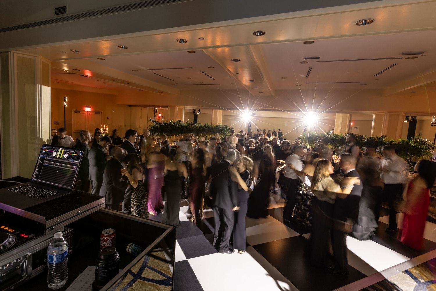 Crowded dance floor at wedding reception with DJ booth visible in the foreground.
