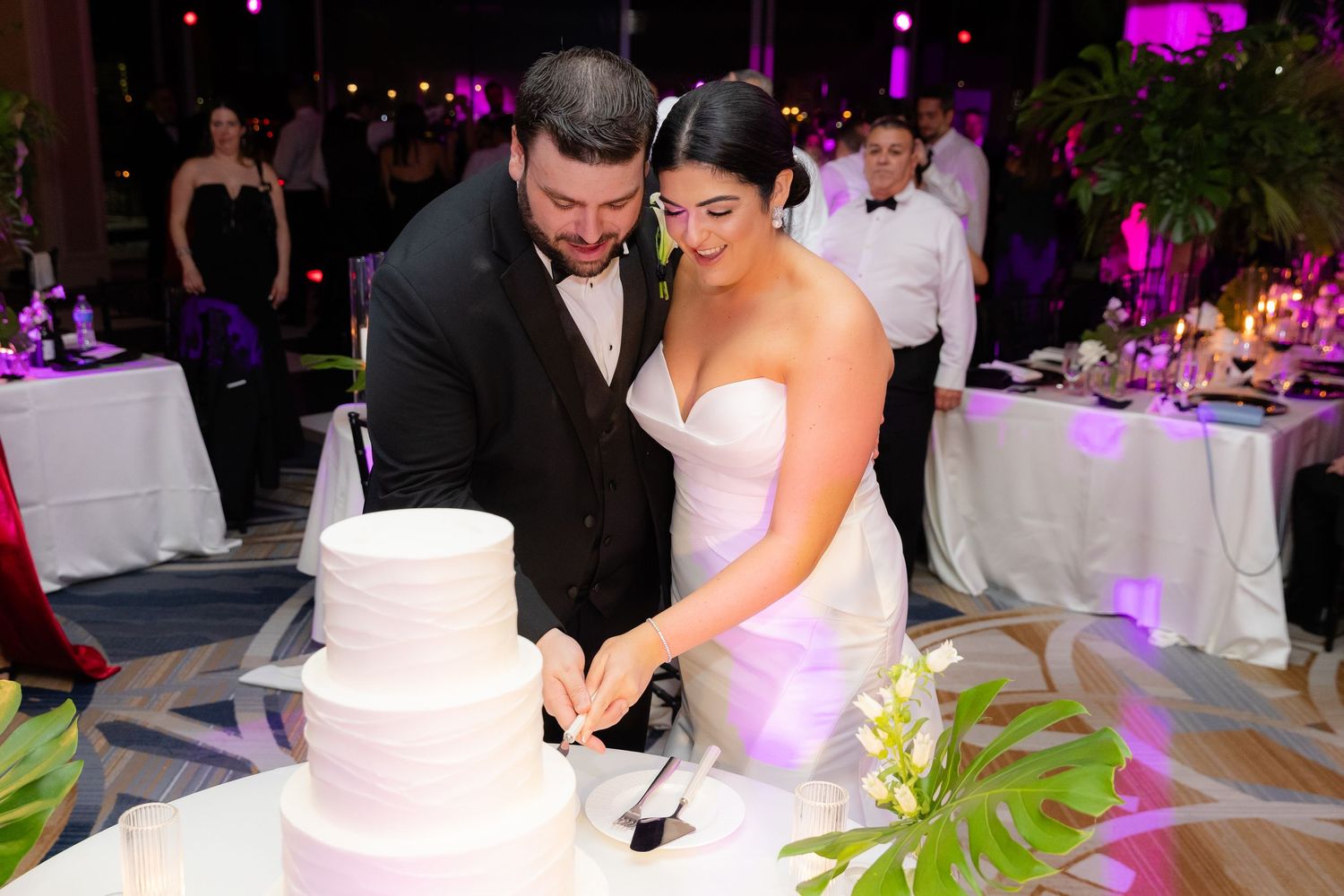 A wedding reception with people dancing and celebrating as purple ambient lighting fills the elegant ballroom.