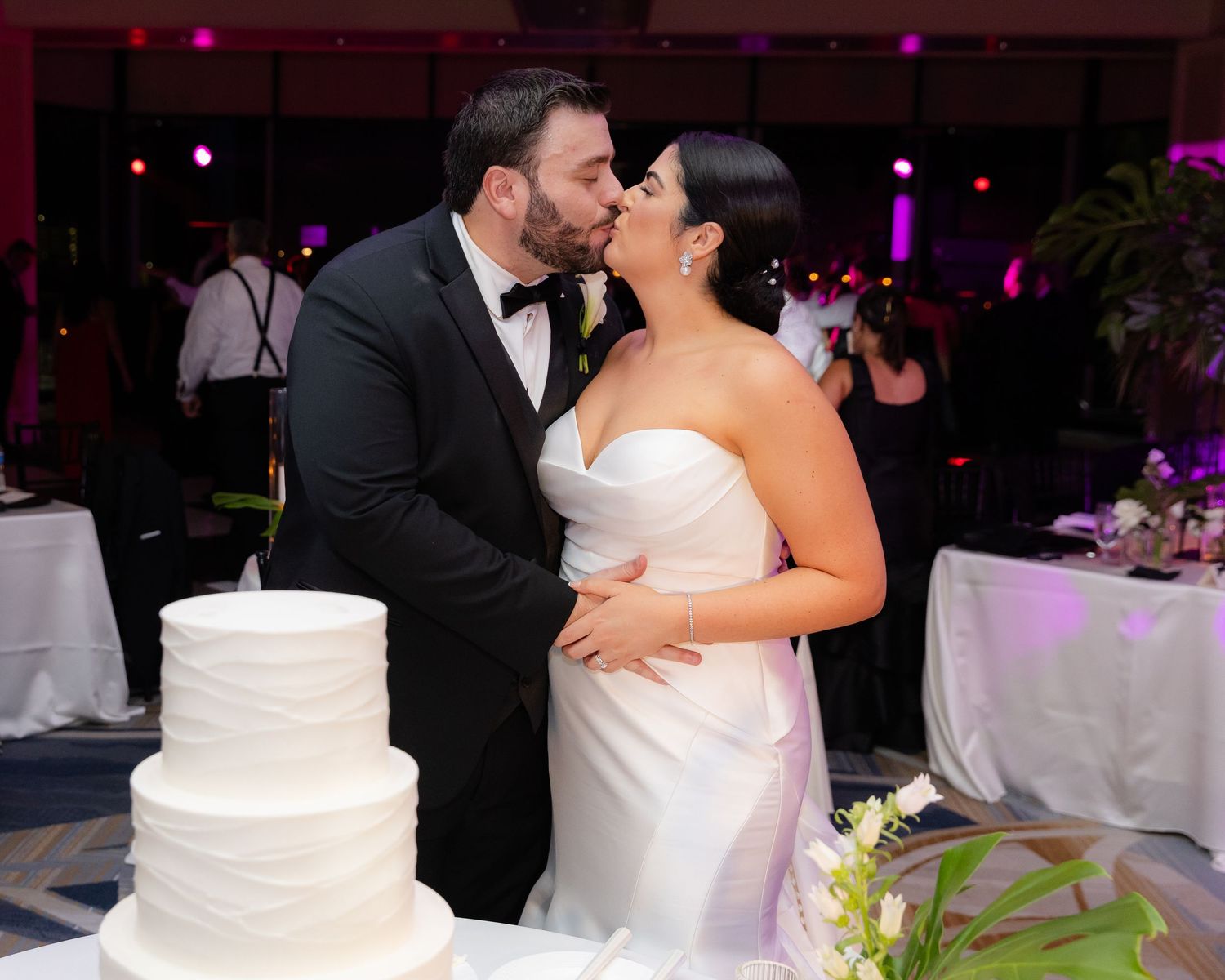 Wedding cake and floral decorations displayed at reception with romantic lighting.