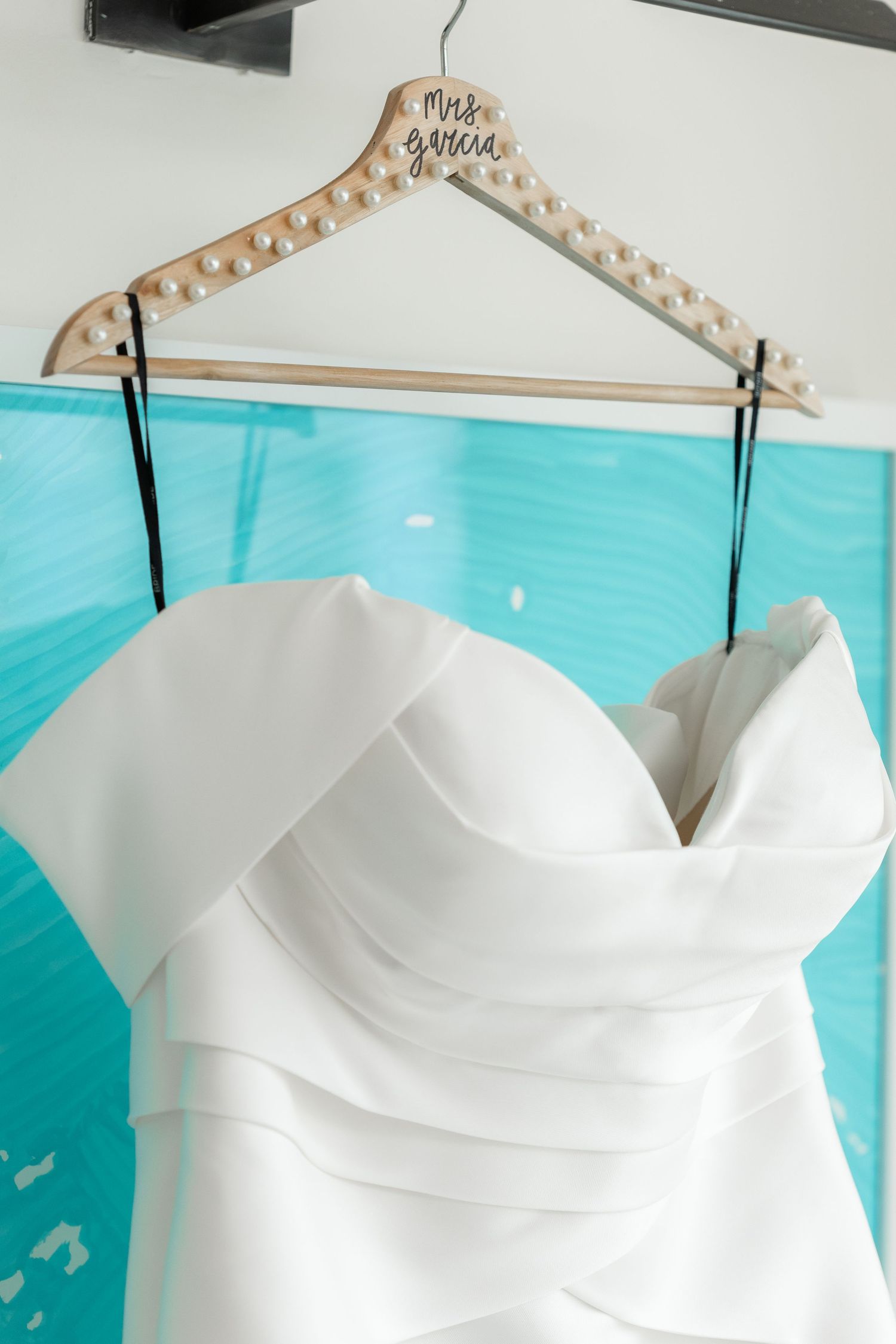 White wedding dress on padded hanger displayed against turquoise blue background.