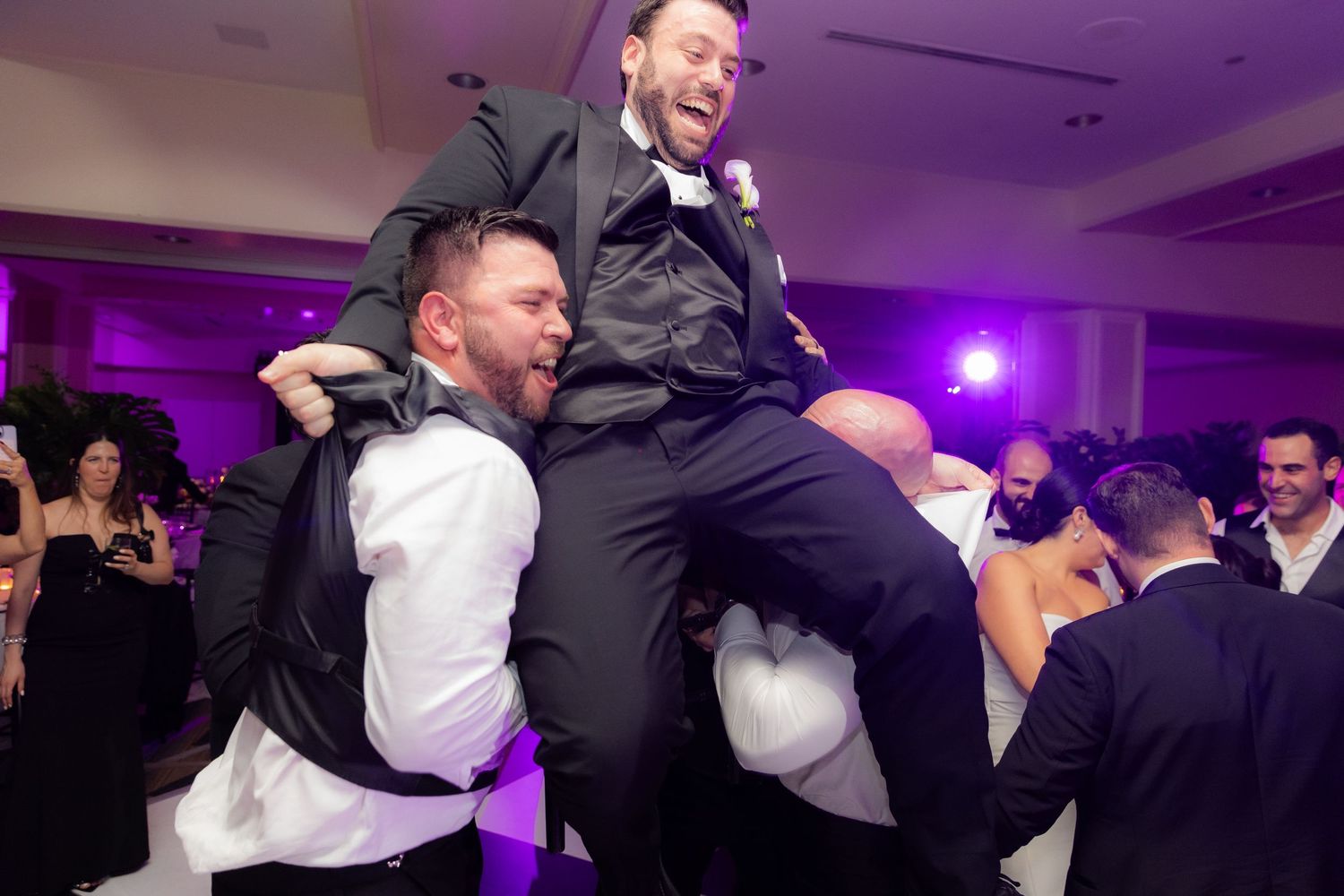 Groomsmen having fun with celebratory lift during wedding reception dance party.