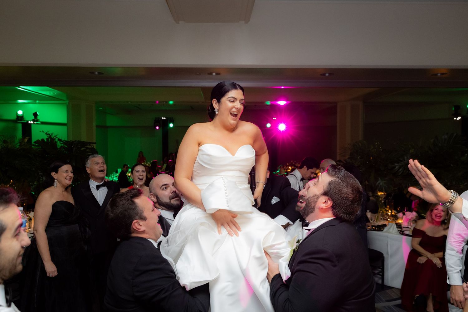 Newlyweds share a joyful dance moment at their reception with guests cheering in the background.