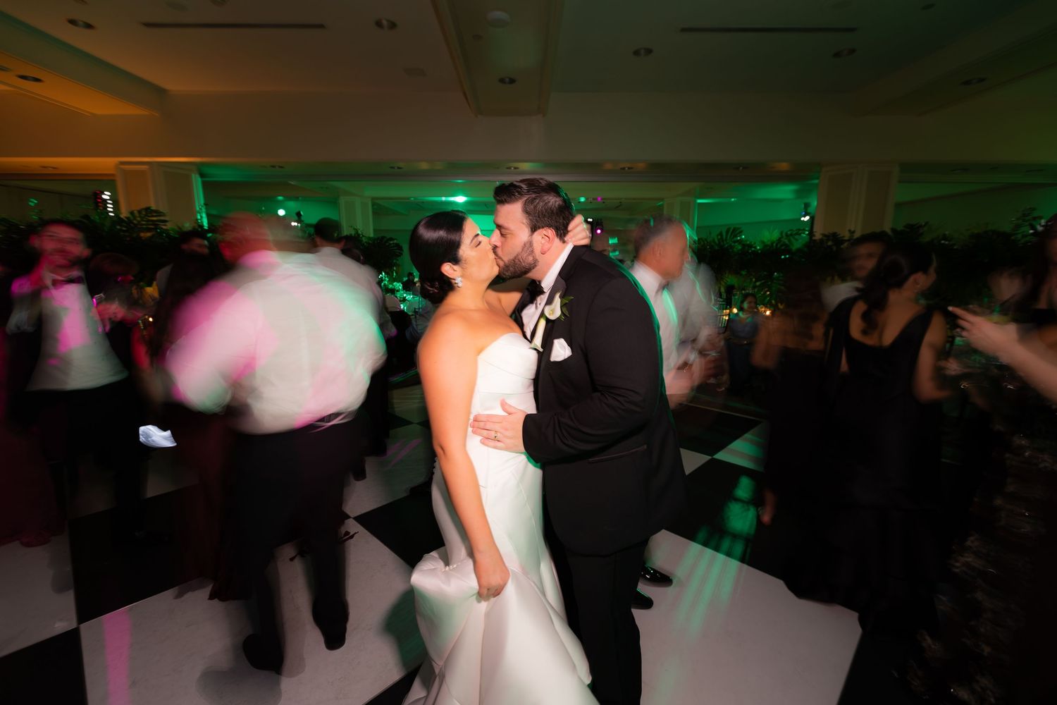 Couples spin across a dimly lit dance floor during an elegant wedding reception celebration.