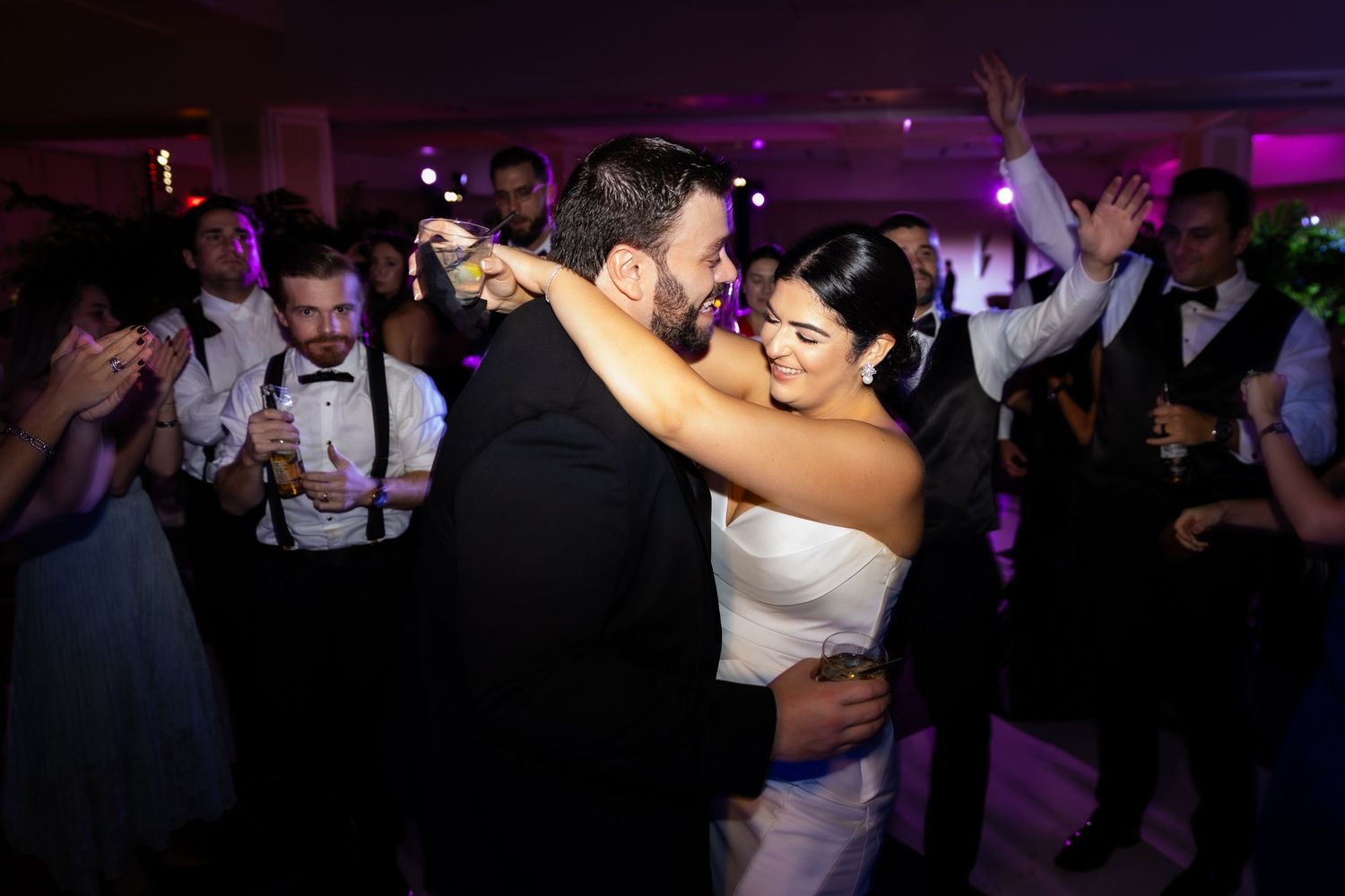 People dancing together at a dimly lit party or celebration with purple lighting and a festive atmosphere.