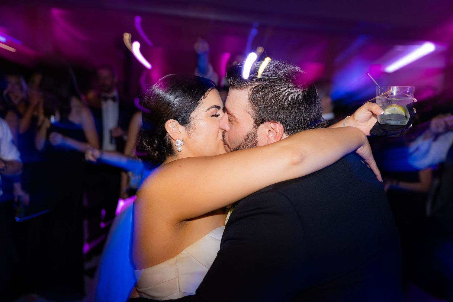 Silhouettes of people dancing and embracing in a nightclub with purple and blue lighting.
