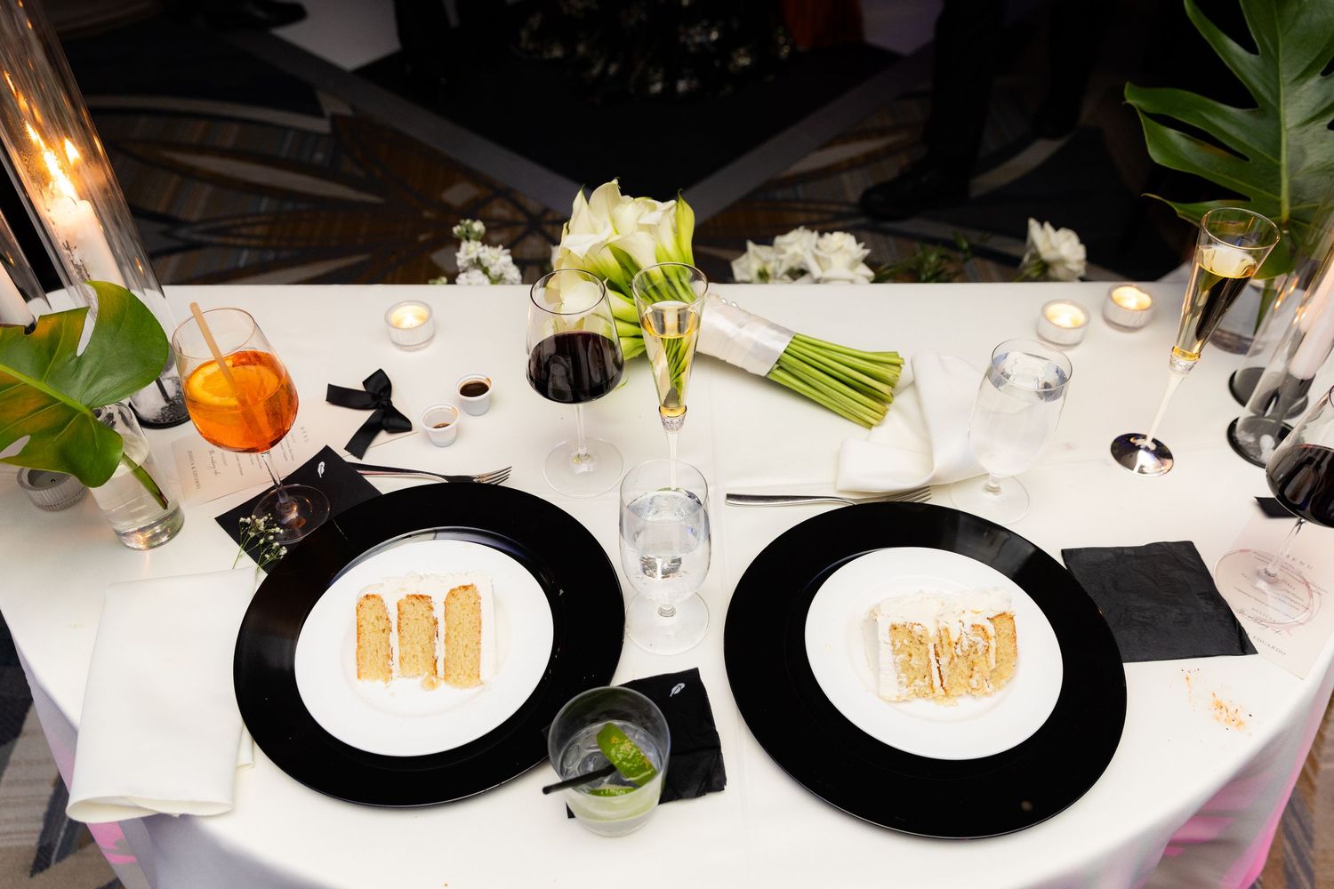 Elegant table settings with black rimmed charger plates and greenery at a formal wedding reception.