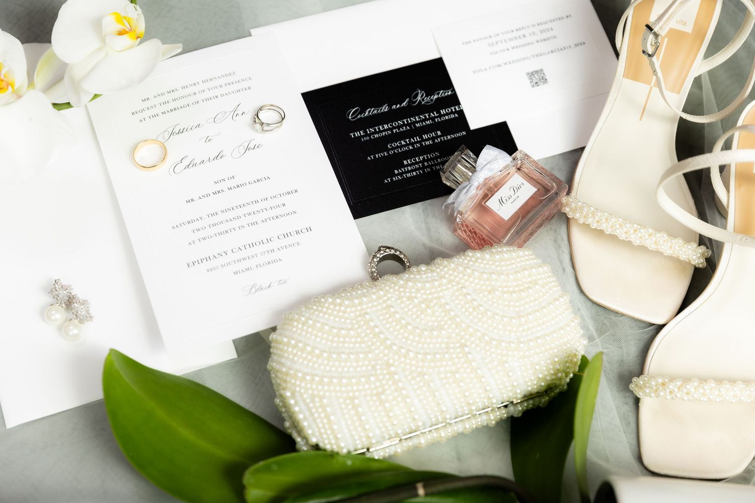 Wedding stationery flat lay with invitations, rings and tropical leaves.
