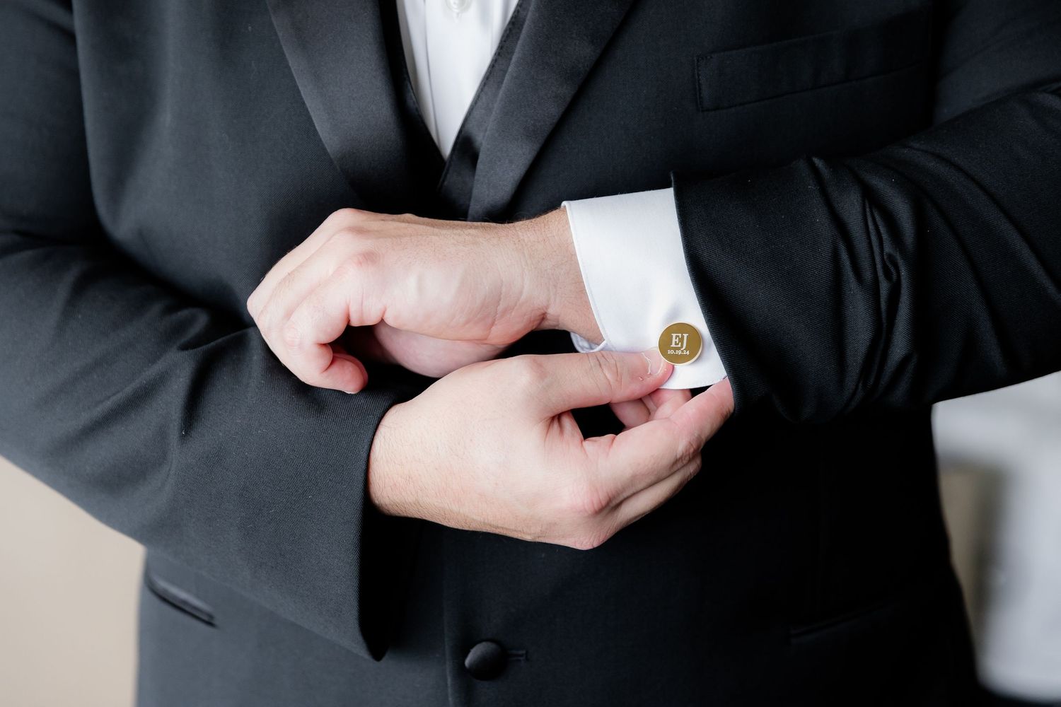 Close-up of hands adjusting a gold cufflink on a formal black suit sleeve.