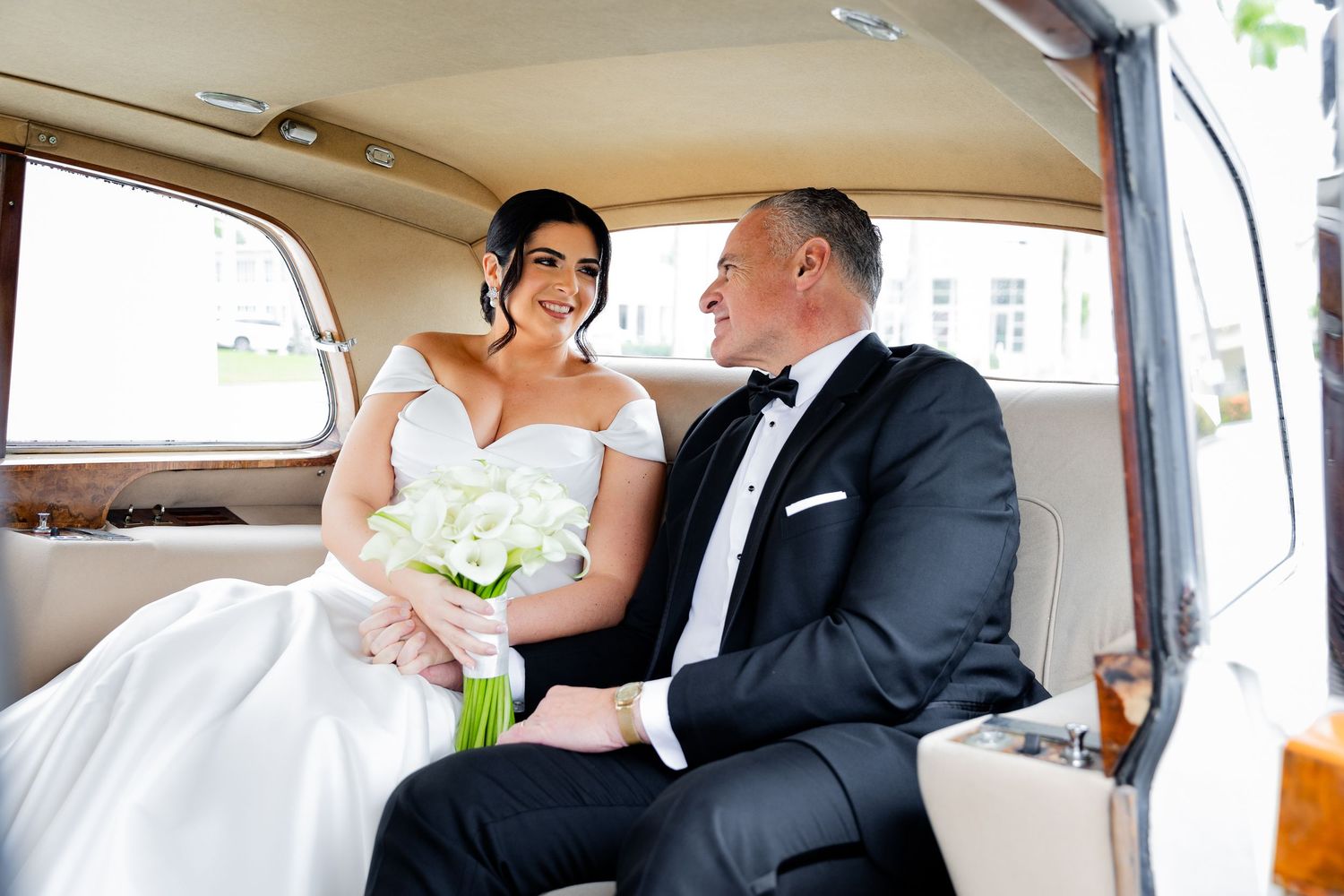 Newlyweds share intimate moment in vintage car with white bouquet.