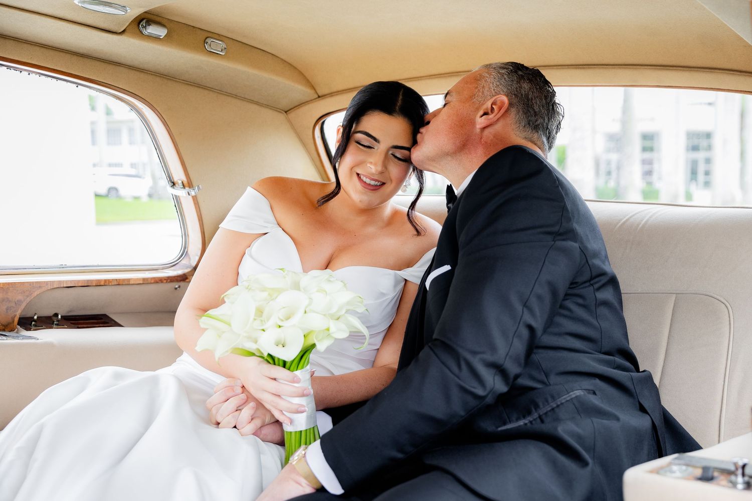 Bride and groom embrace while sitting in an elegant vintage car interior.