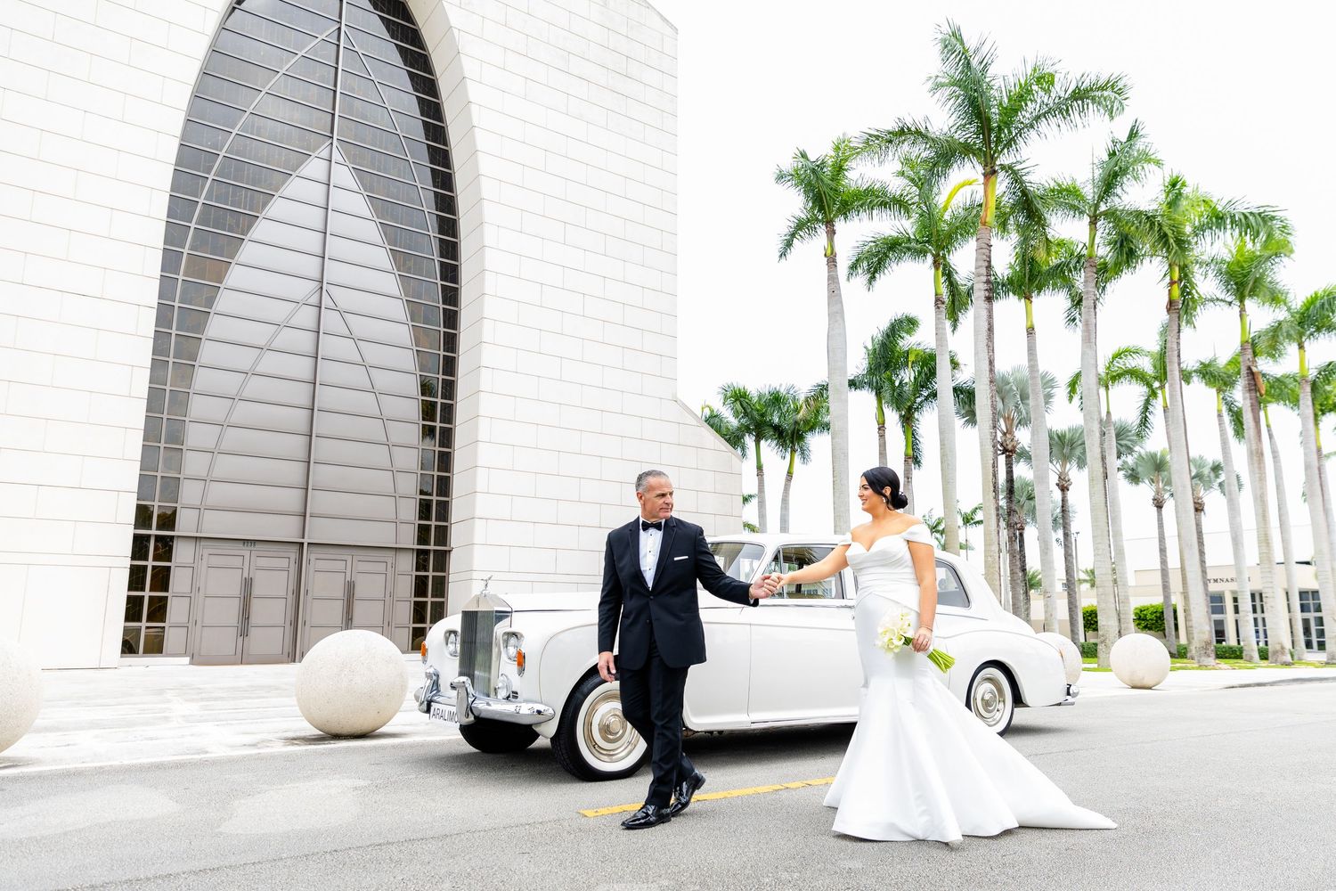Elegant white wedding ceremony location with rows of tall palm trees lining a white architectural backdrop.