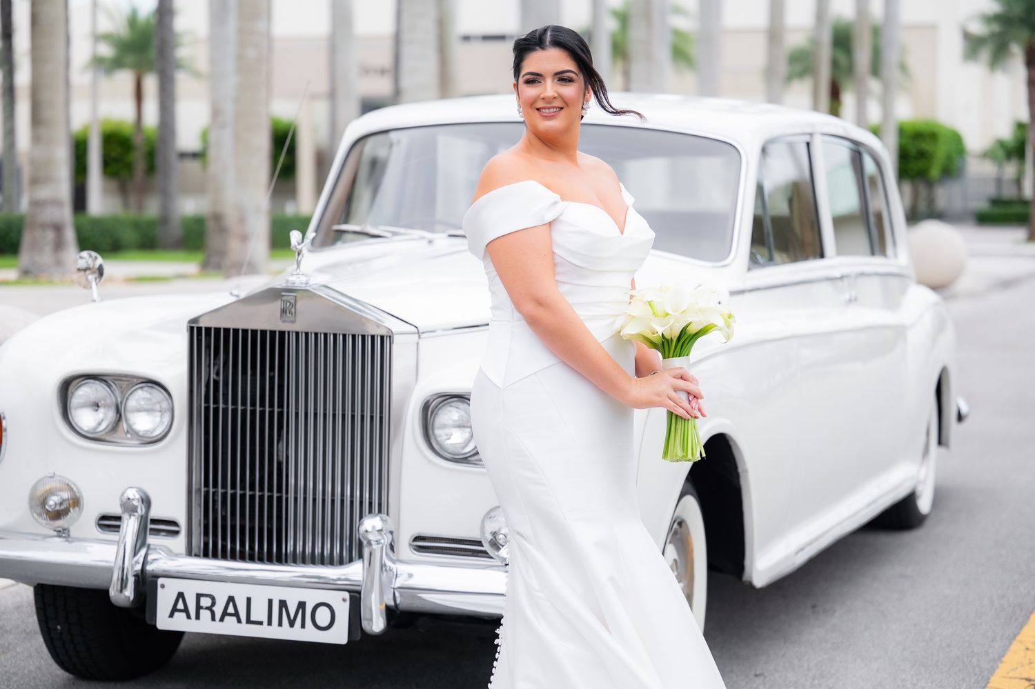 Classic white Rolls Royce limousine with 'ARALIMO' plate parked outside.
