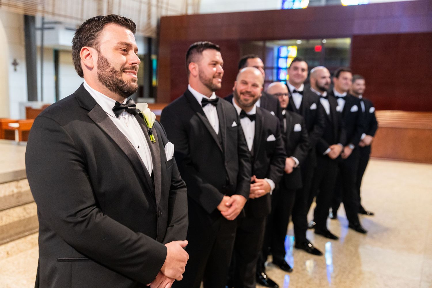 Groomsmen in black tuxedos lined up in formation at formal event.