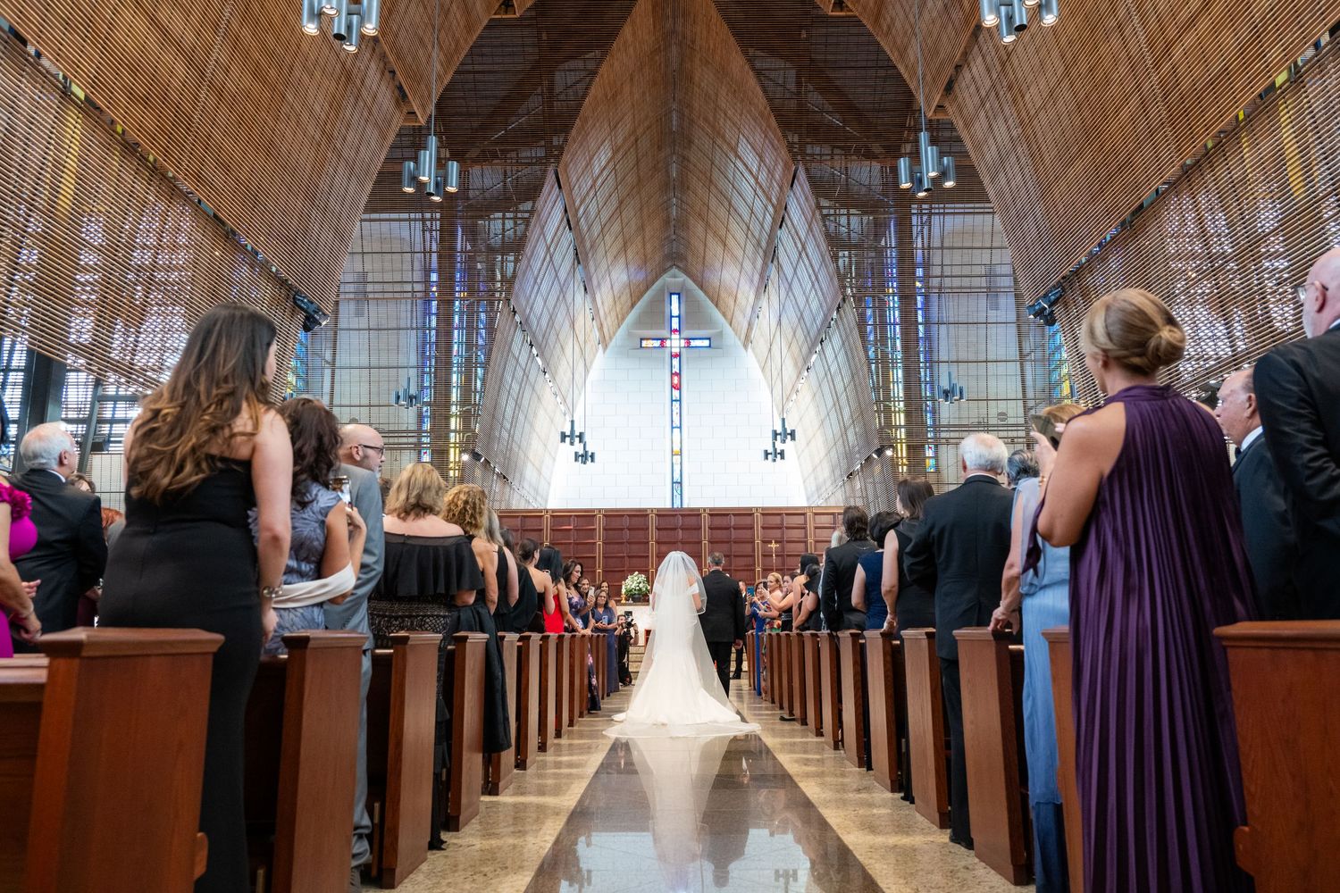 Long church aisle with wooden pews and ornate architecture during a wedding ceremony.