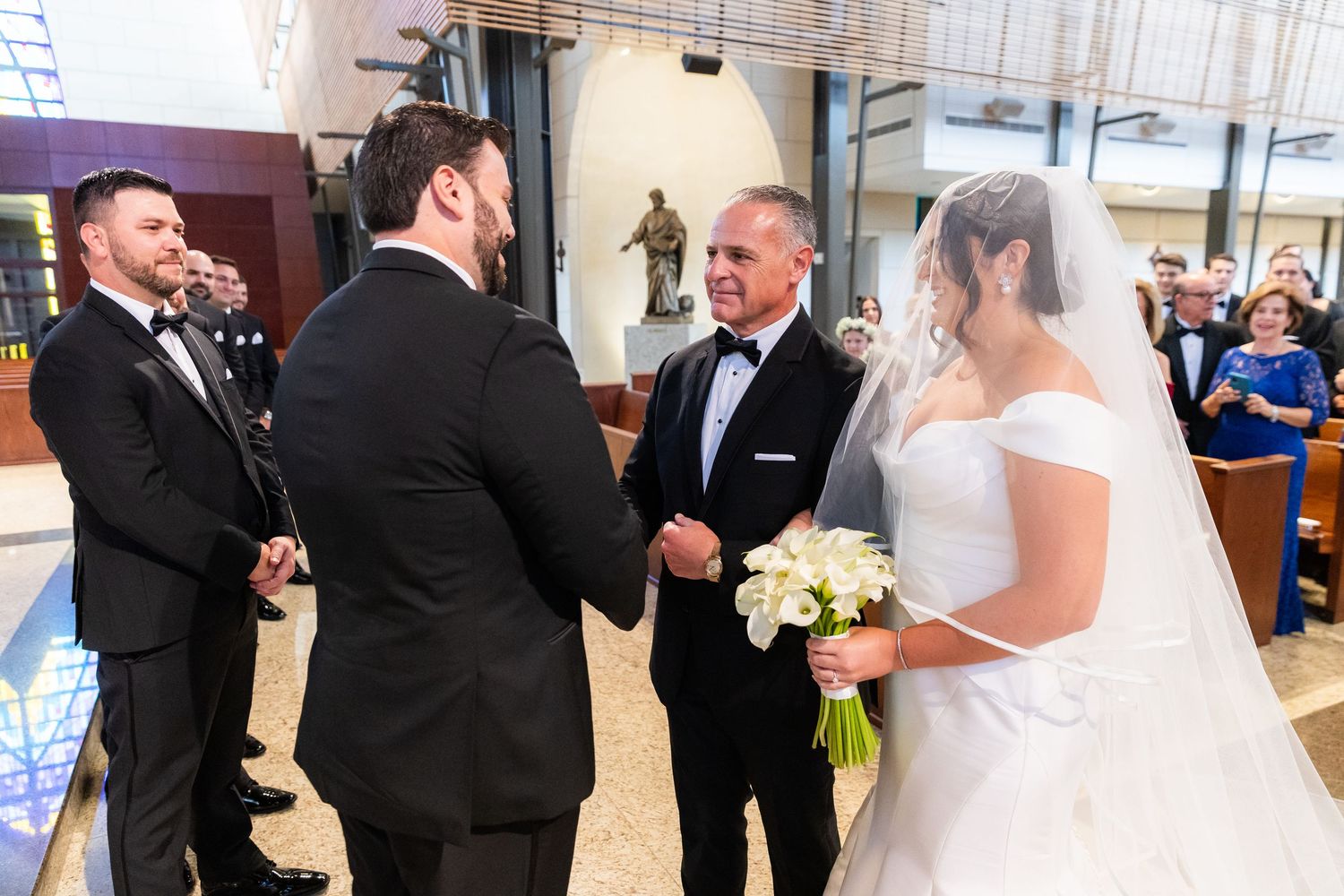 Wedding ceremony exchange in church interior with groomsmen and bride.