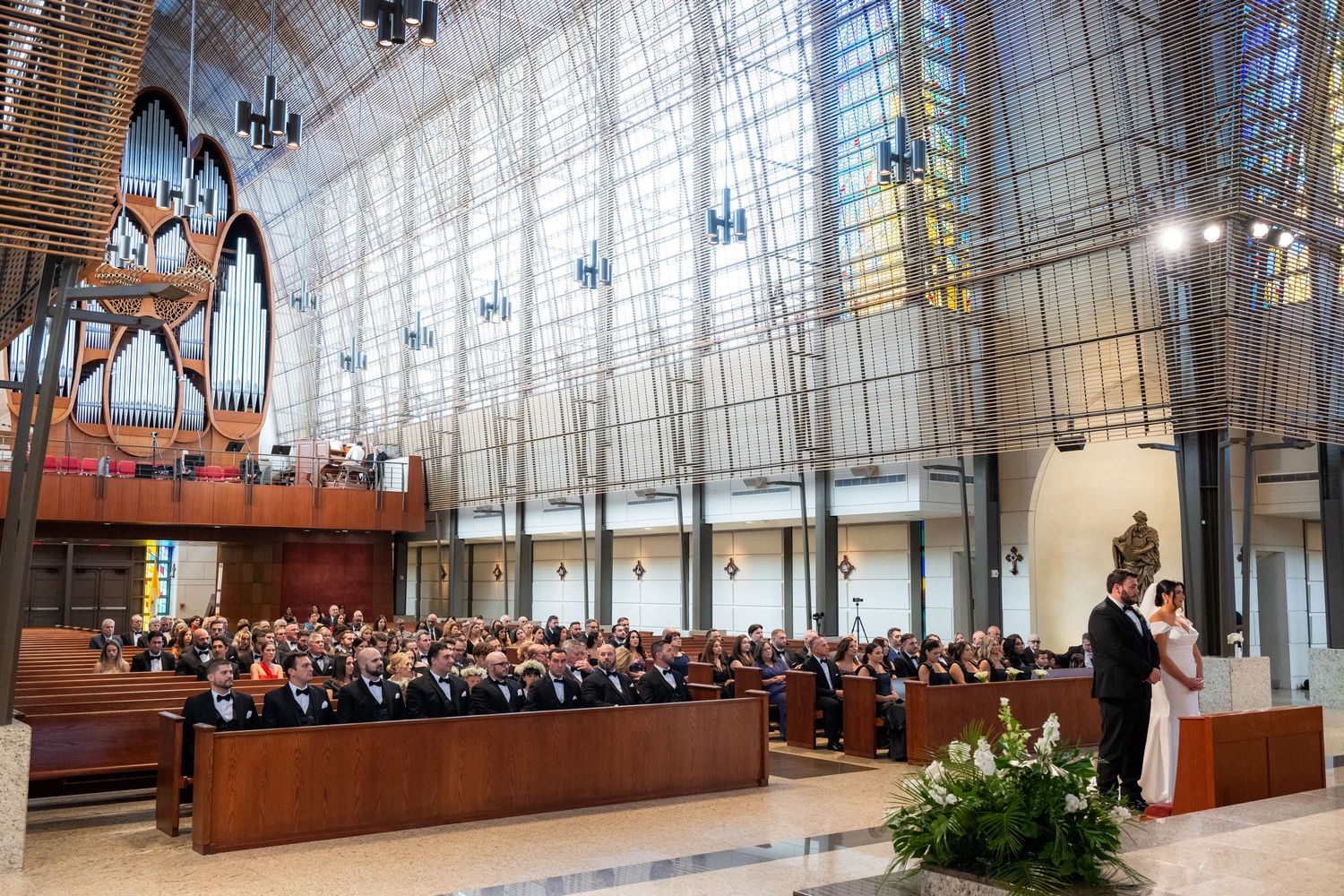 Modern church sanctuary with soaring glass walls and wooden pews filled with congregants during a wedding ceremony.