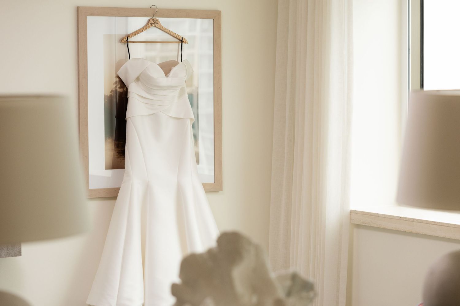 White wedding dress hanging in window light before ceremony.