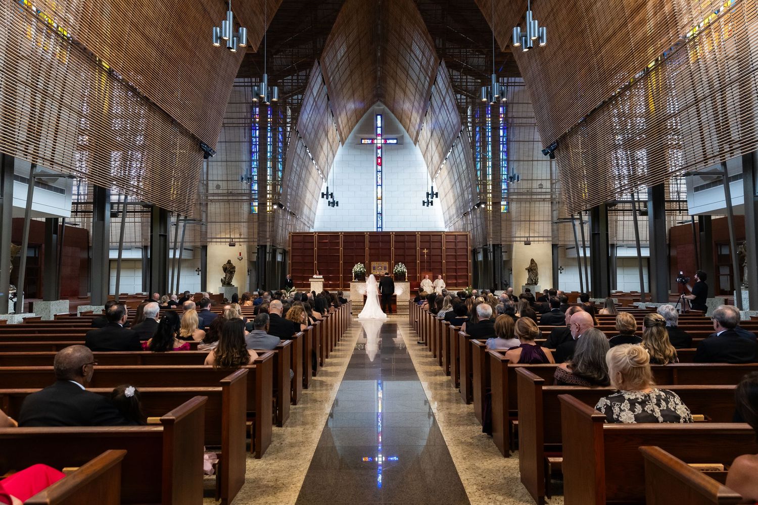 Gothic church interior with stained glass windows and wooden pews leading to illuminated altar.