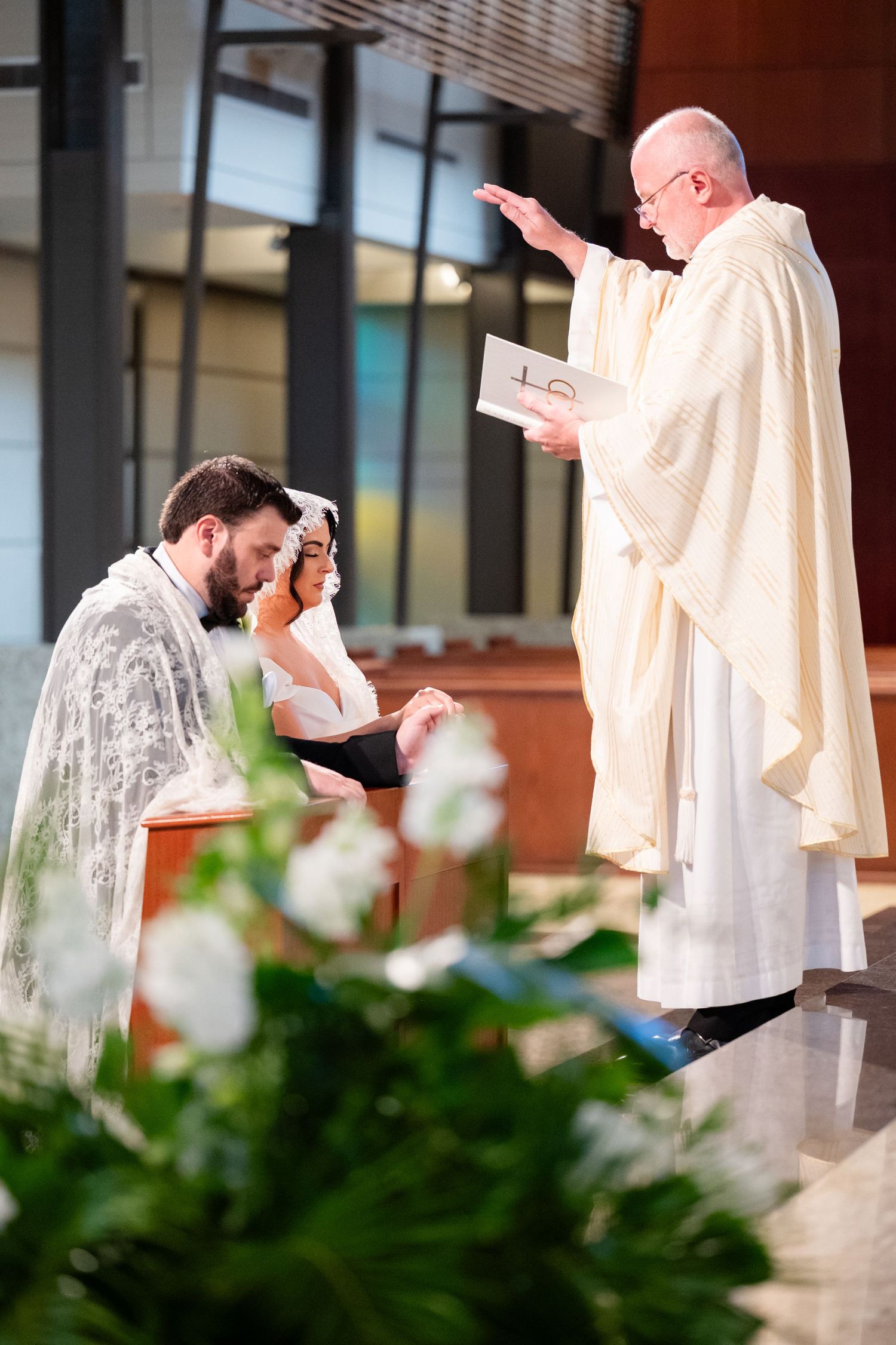 Religious ceremony taking place inside a church with priest in white robes performing blessings.