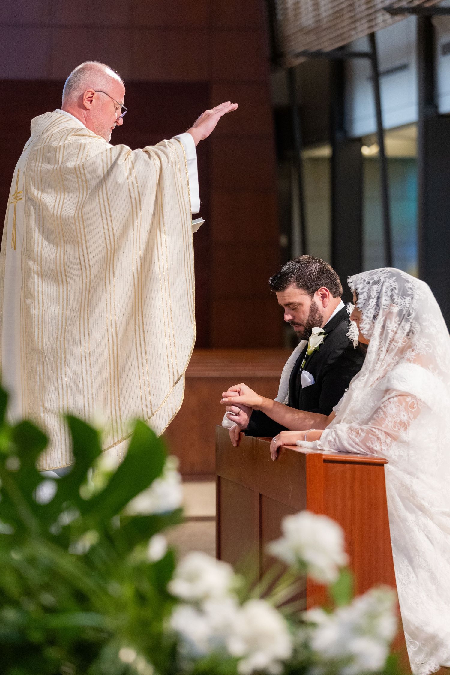 Religious wedding ceremony with priest performing blessing at wooden altar.