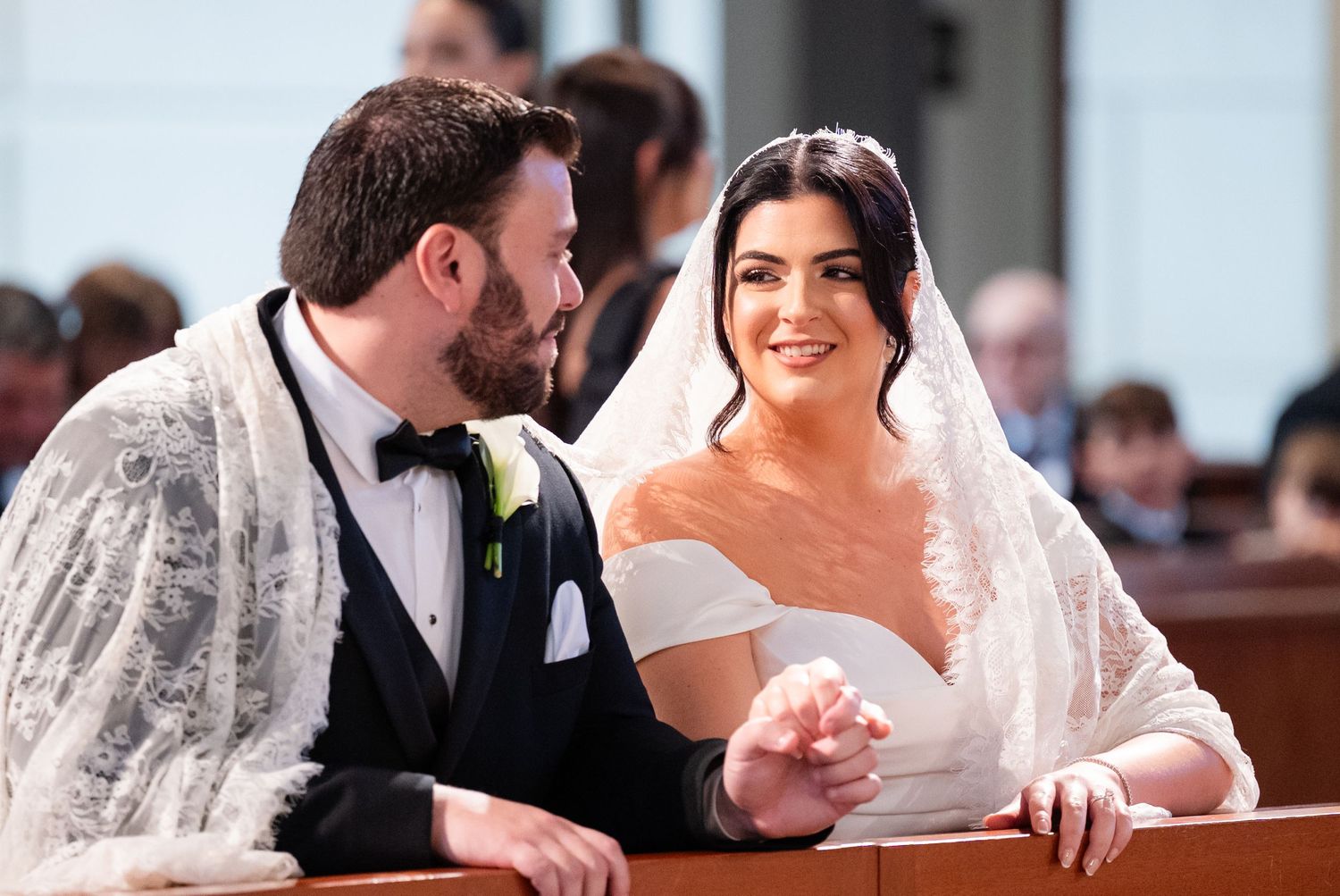 Elegant couple sharing a moment in church pews during wedding ceremony.