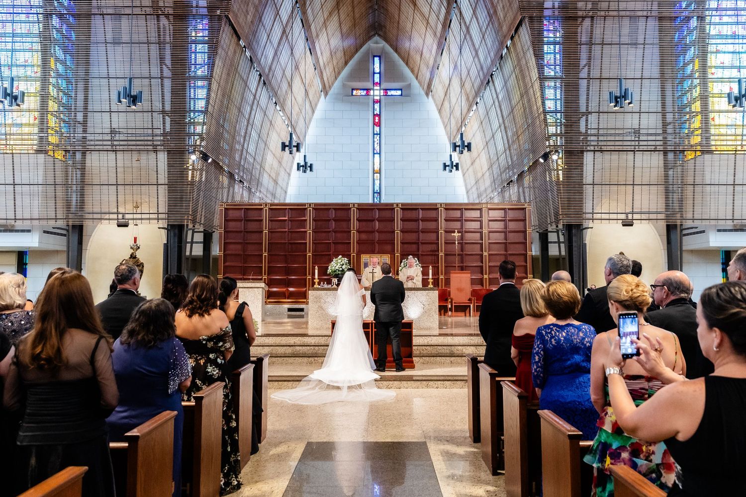Natural light streams through stained glass windows in a magnificent cathedral during wedding ceremony.