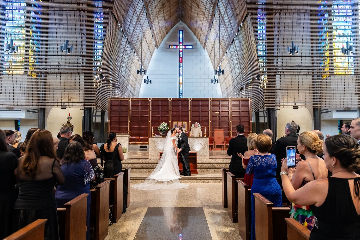 Wedding ceremony in modern church with dramatic stained glass windows and vaulted ceiling.