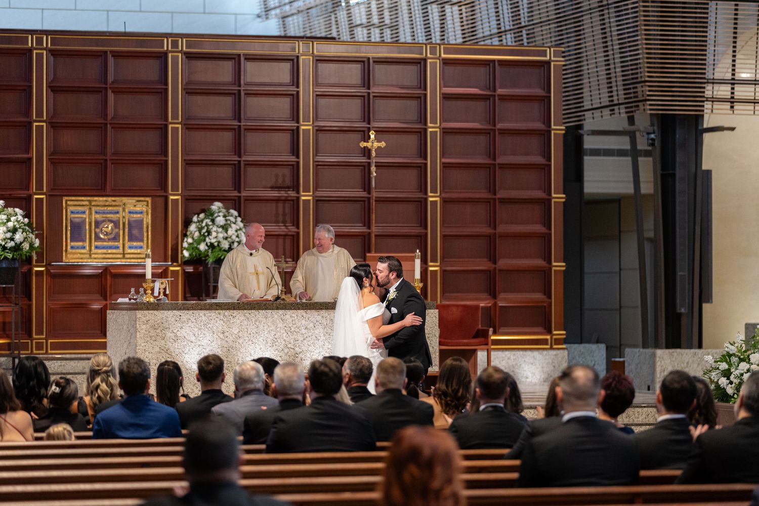 Traditional church wedding ceremony with wooden pews and stained glass windows in warm lighting.