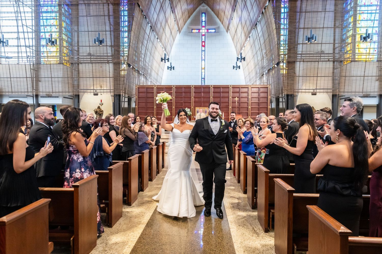 Wedding recessional in beautiful church with stained glass windows and cheering guests.