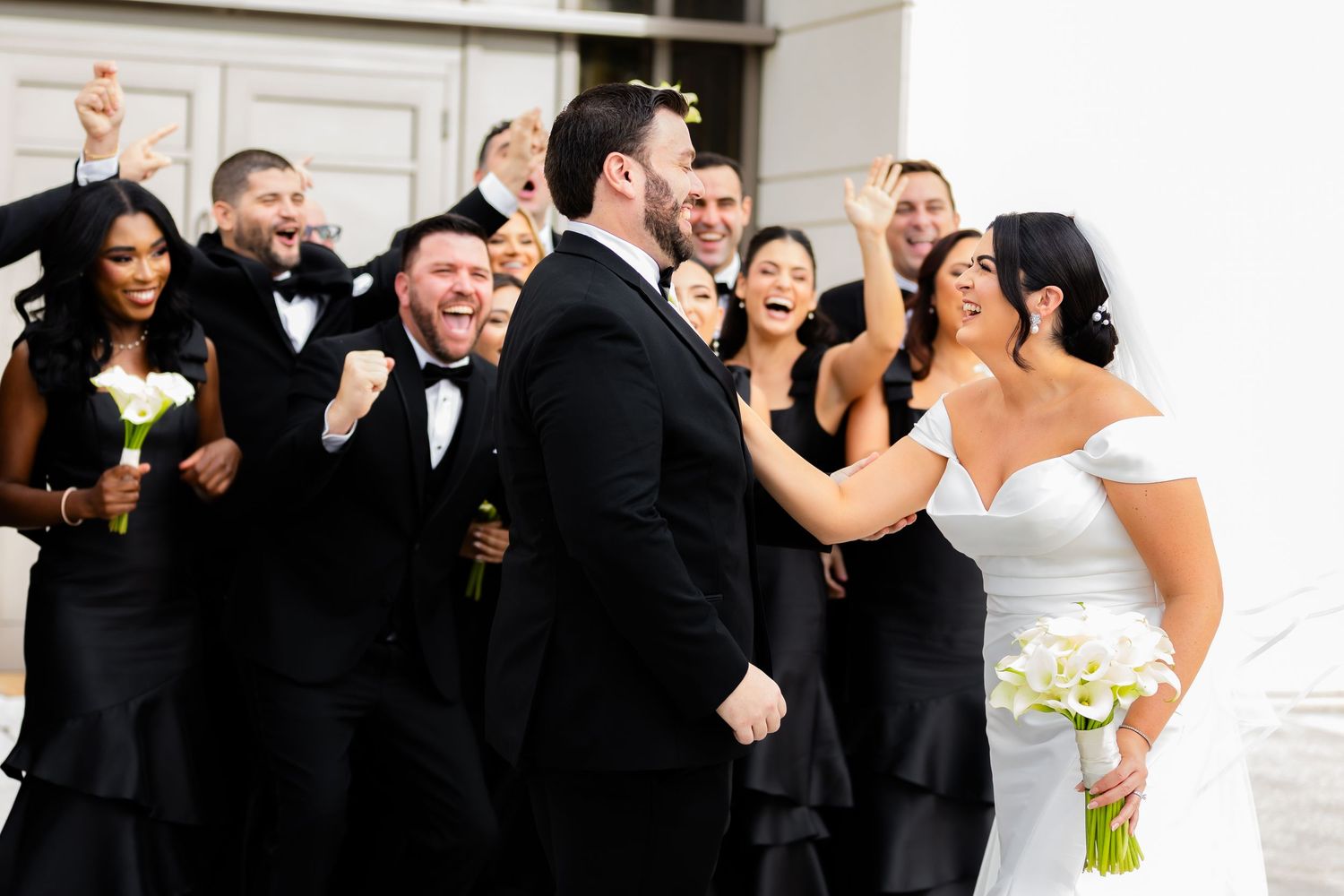 Wedding party in black attire laughing together outdoors.
