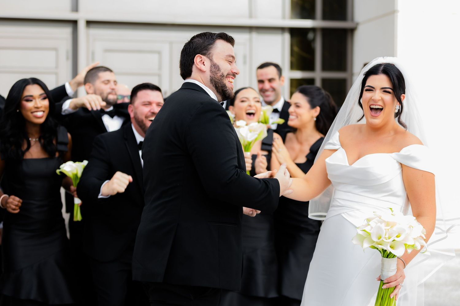 Wedding party celebrating and laughing together outside white building.