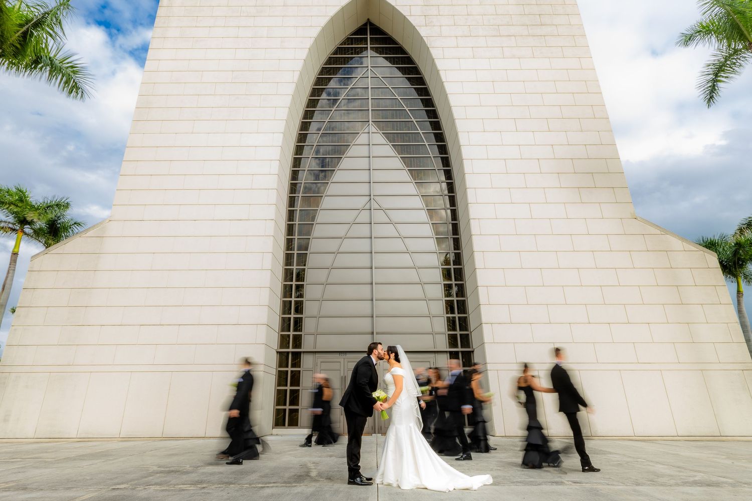 Modern white church exterior with Gothic-style arched entrance and palm trees.