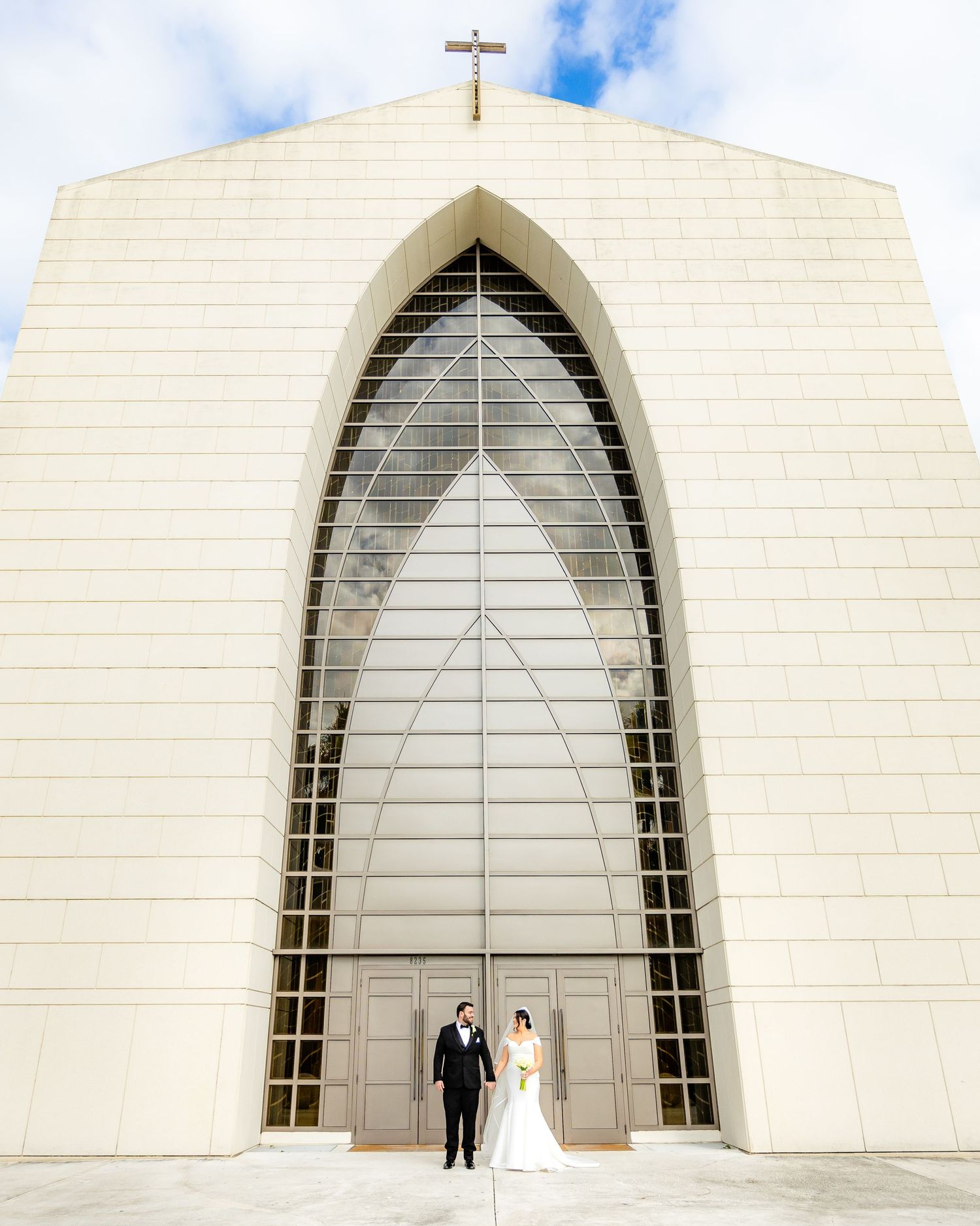 Modern white church exterior with geometric arches and cross against blue sky.