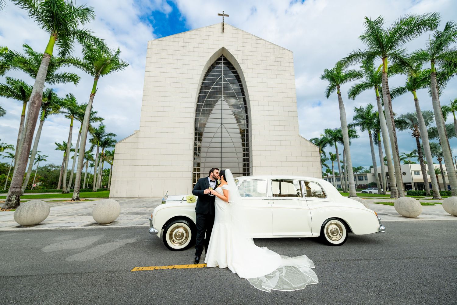 White church with palm trees and vintage car creating a tropical wedding setting.