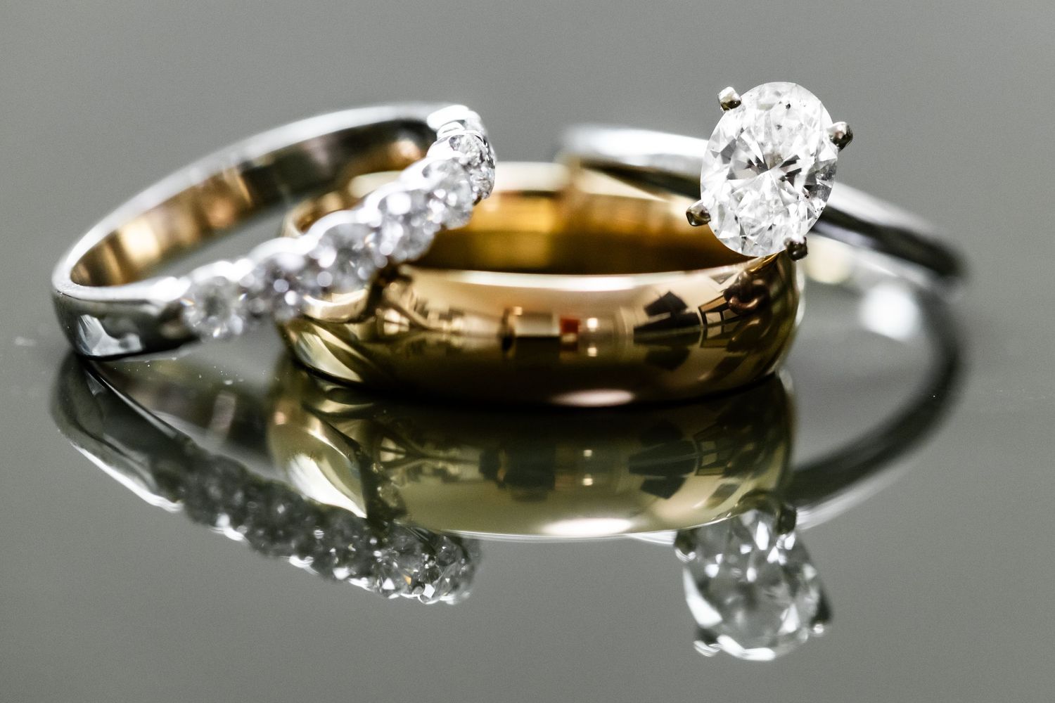 Close-up macro shot of diamond engagement rings and wedding bands on reflective surface.