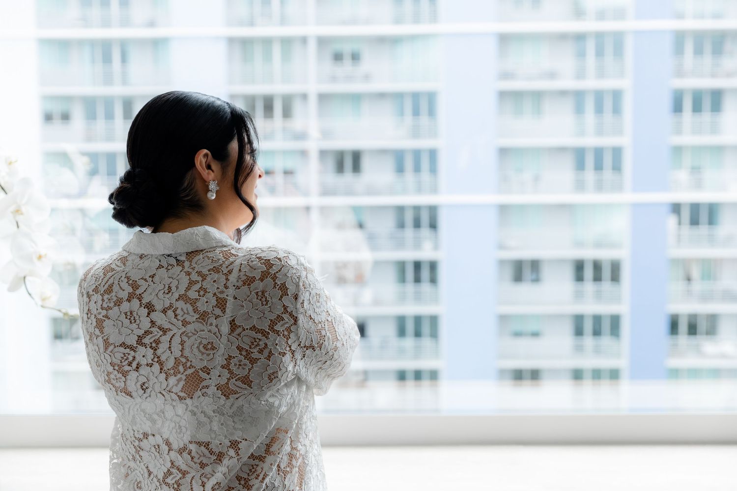 A luxurious white lace bridal gown is showcased against a modern high-rise building backdrop.