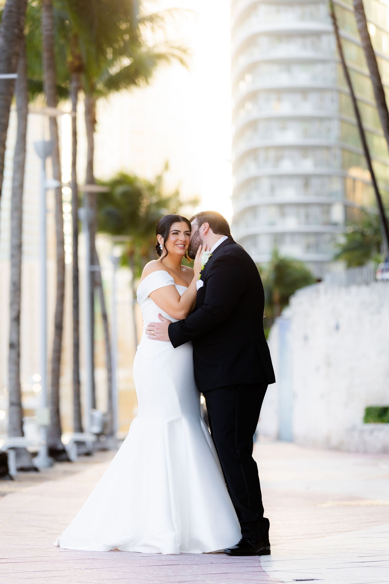 Romantic wedding couple moment along a palm tree-lined pathway.