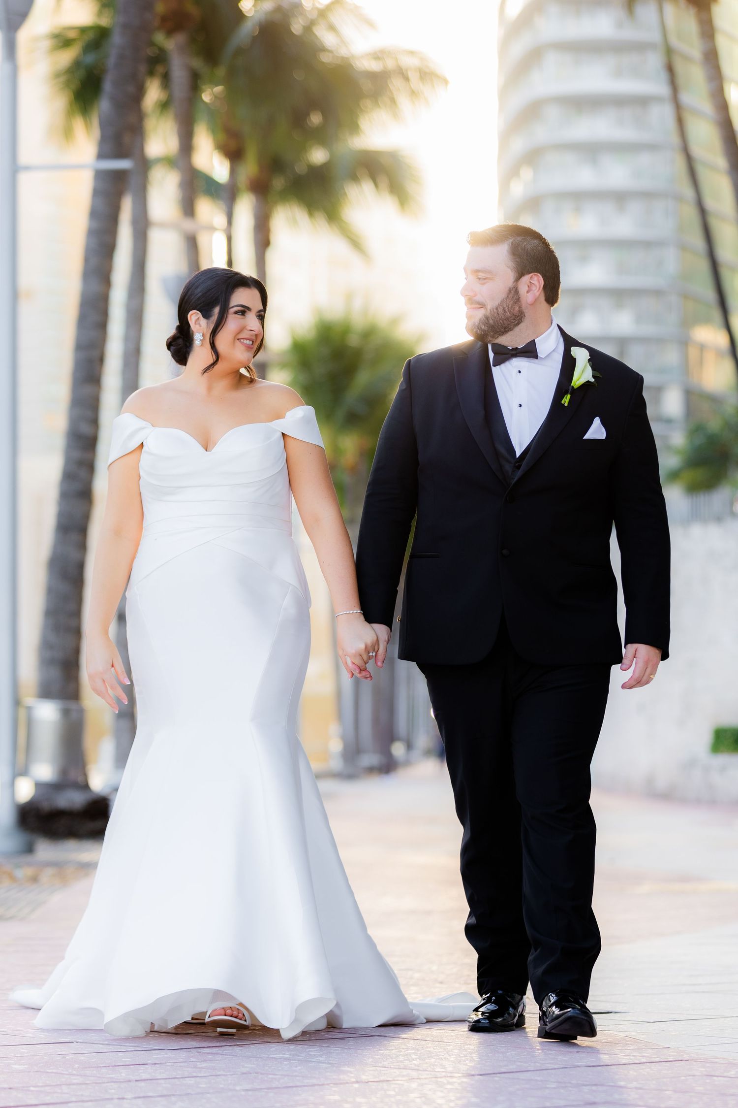 Wedding couple walking among tropical palm trees at sunset.