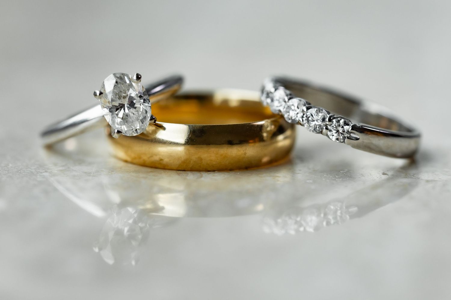 Close-up of elegant wedding rings including diamond engagement ring and gold band on light gray surface.