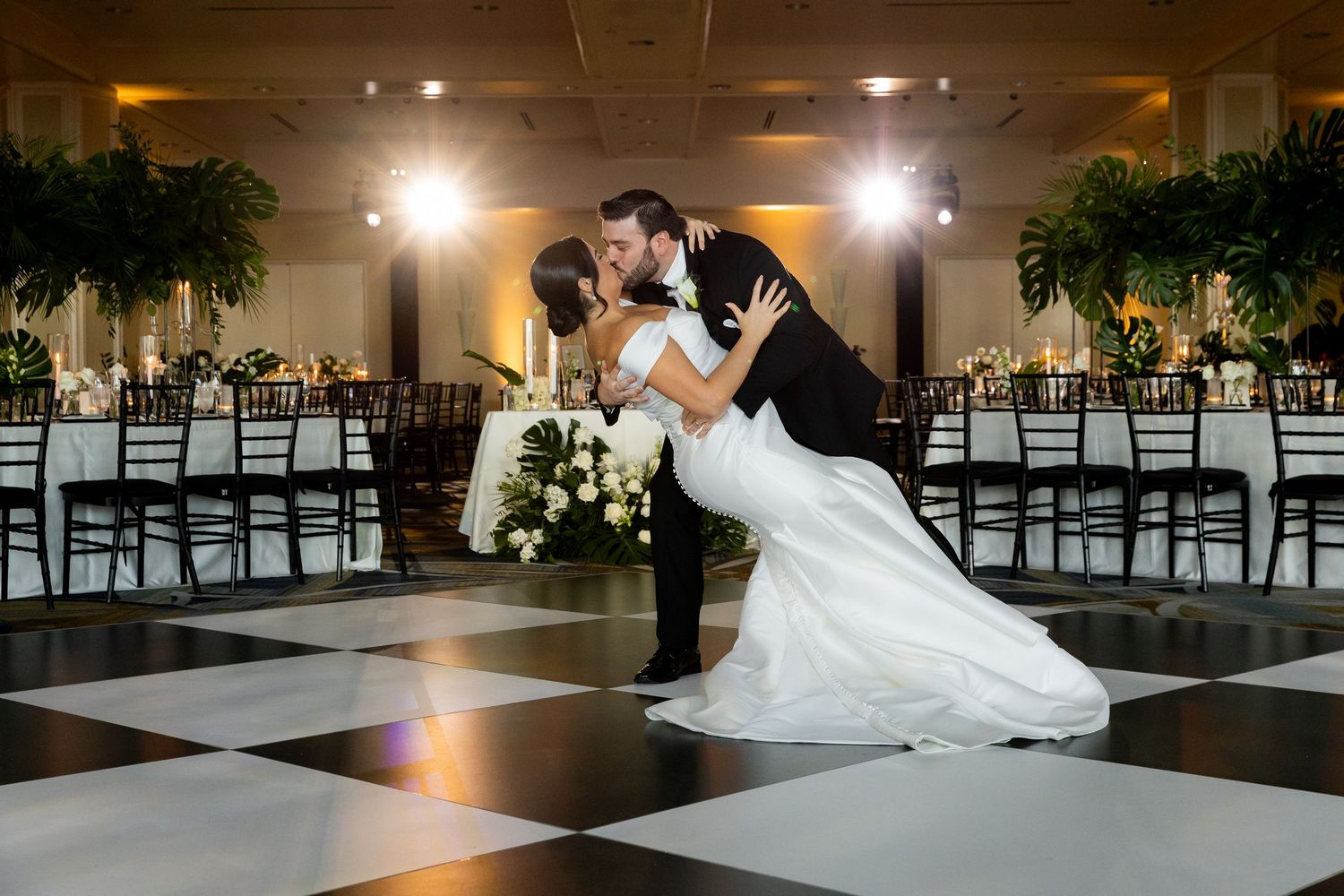 A couple performing their first dance on a glossy black dance floor with dramatic lighting in an elegant venue.