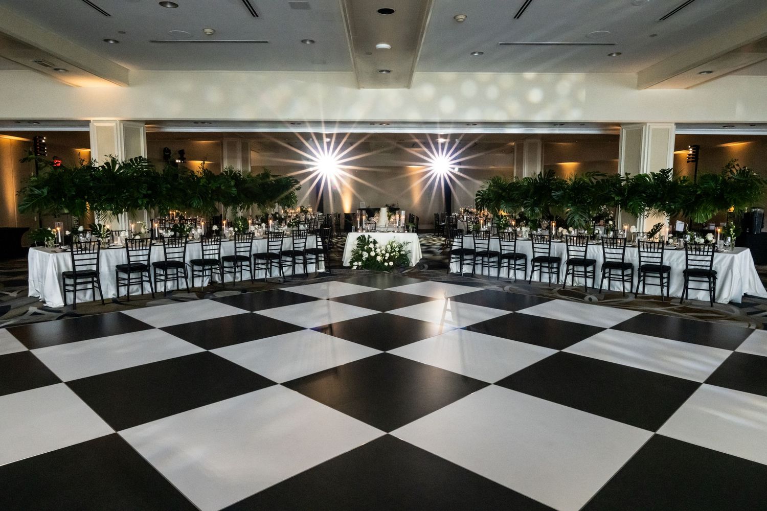 Wide angle view of a black and white checkered dance floor in an elegant ballroom with recessed lighting.