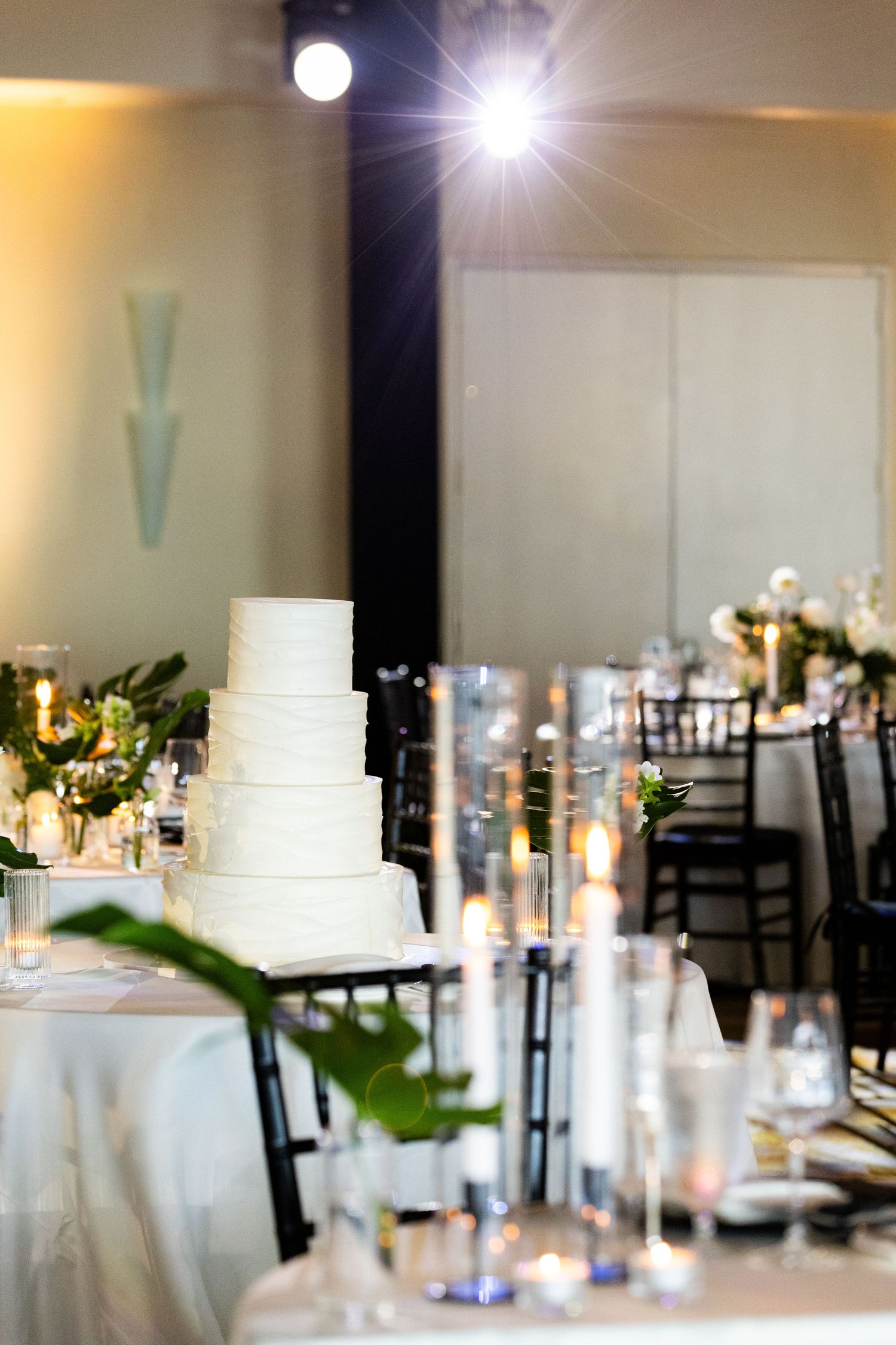 White wedding cake displayed in an elegant reception room with soft lighting and table settings.