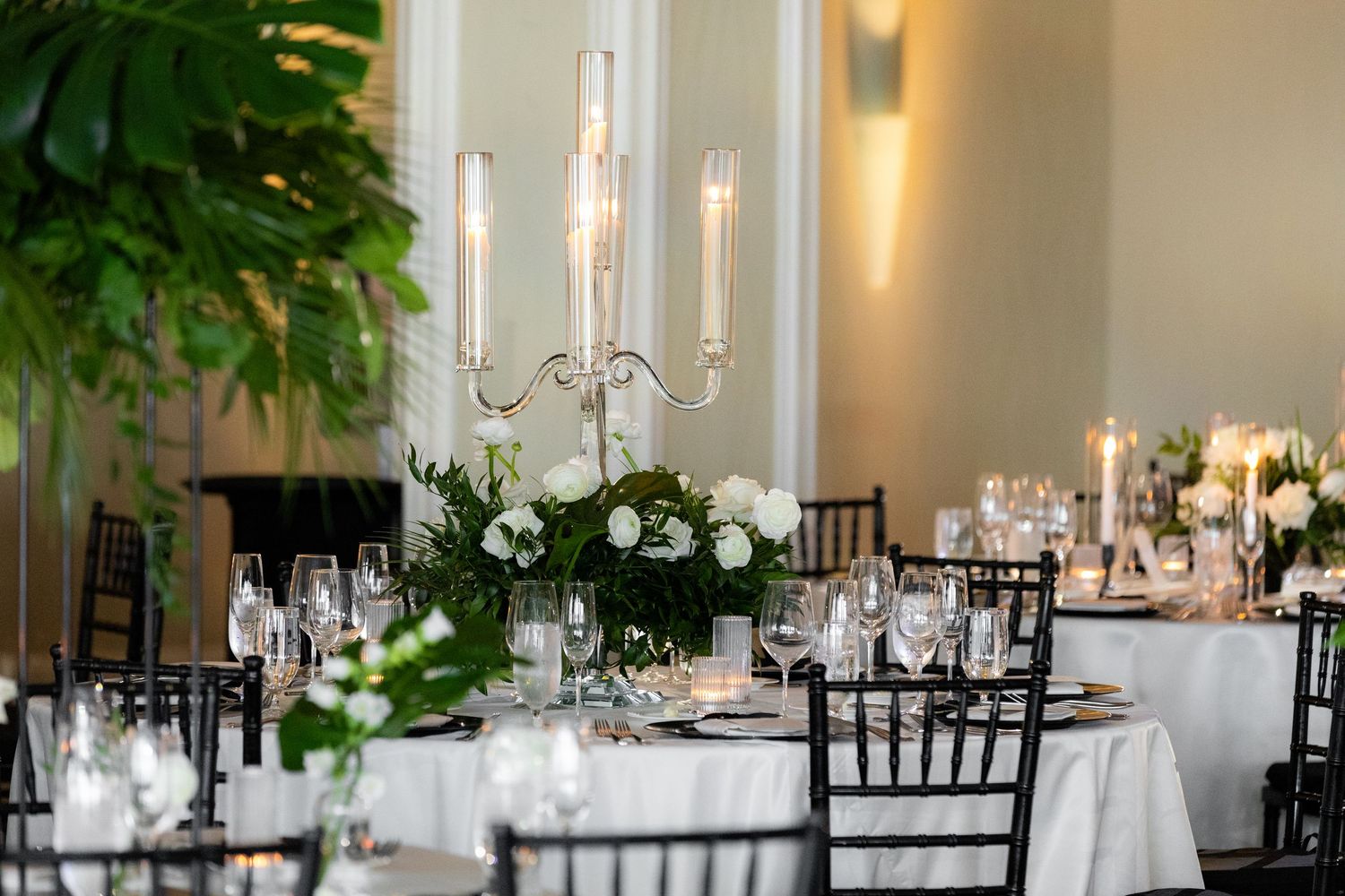 Elegant wedding reception venue with black chairs, white linens, and lush green floral arrangements.
