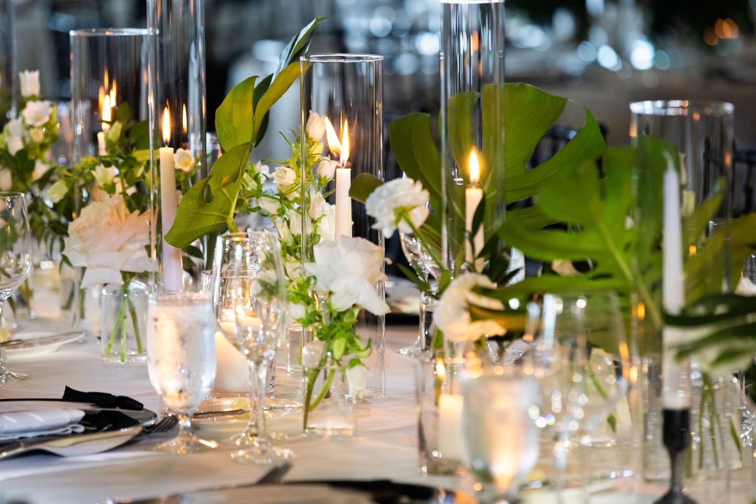 Elegant wedding reception table settings with glowing candles and green floral centerpieces.