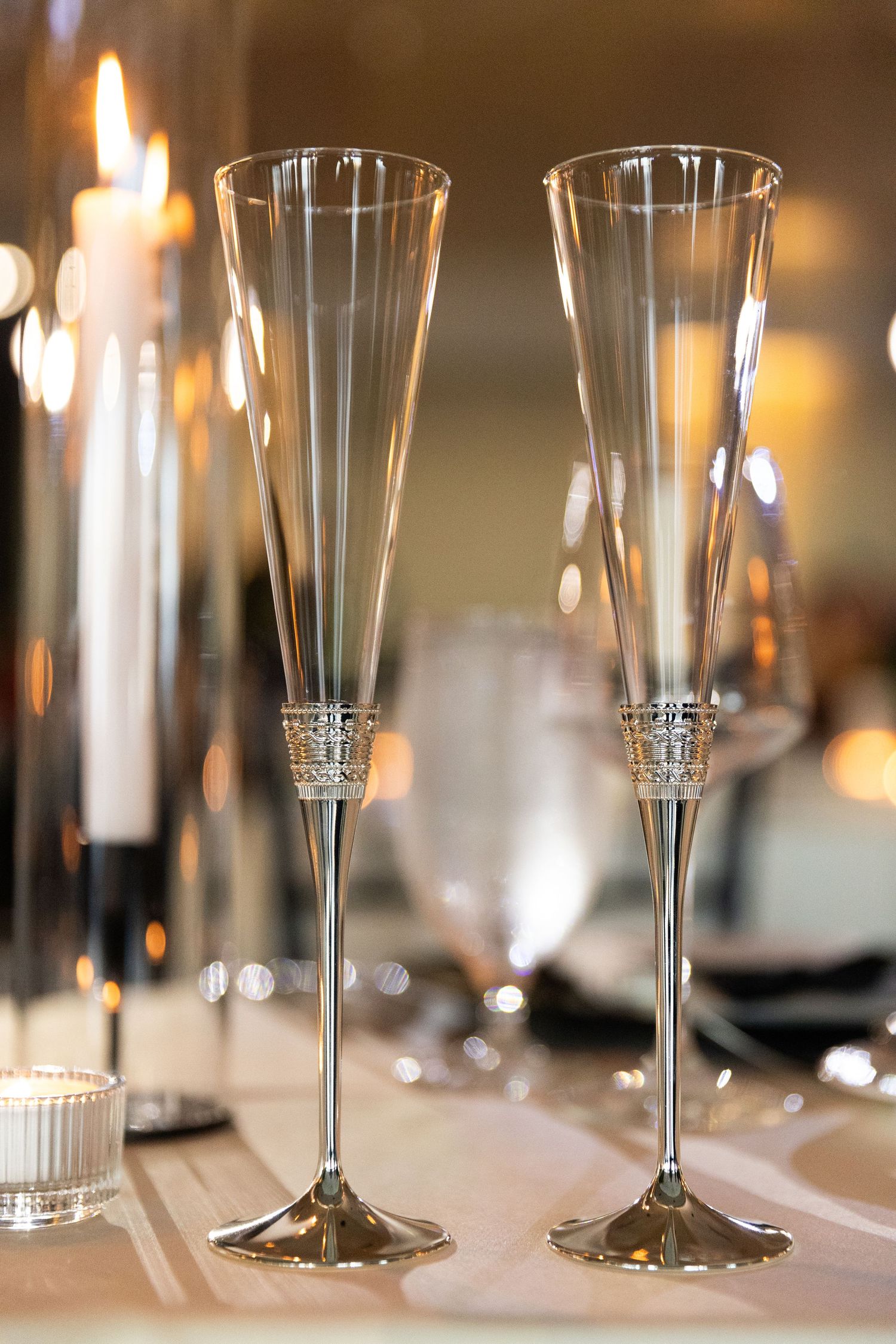 Elegant champagne flutes lined up on a formal dining table with soft candlelight in the background.