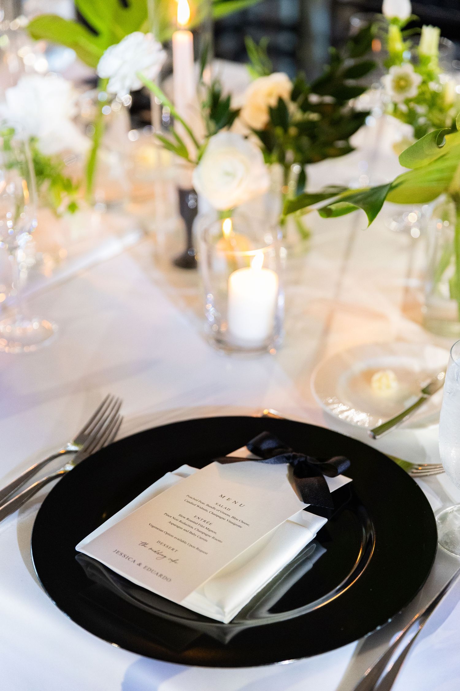 Black and white place settings with menu cards on a formal wedding reception table.