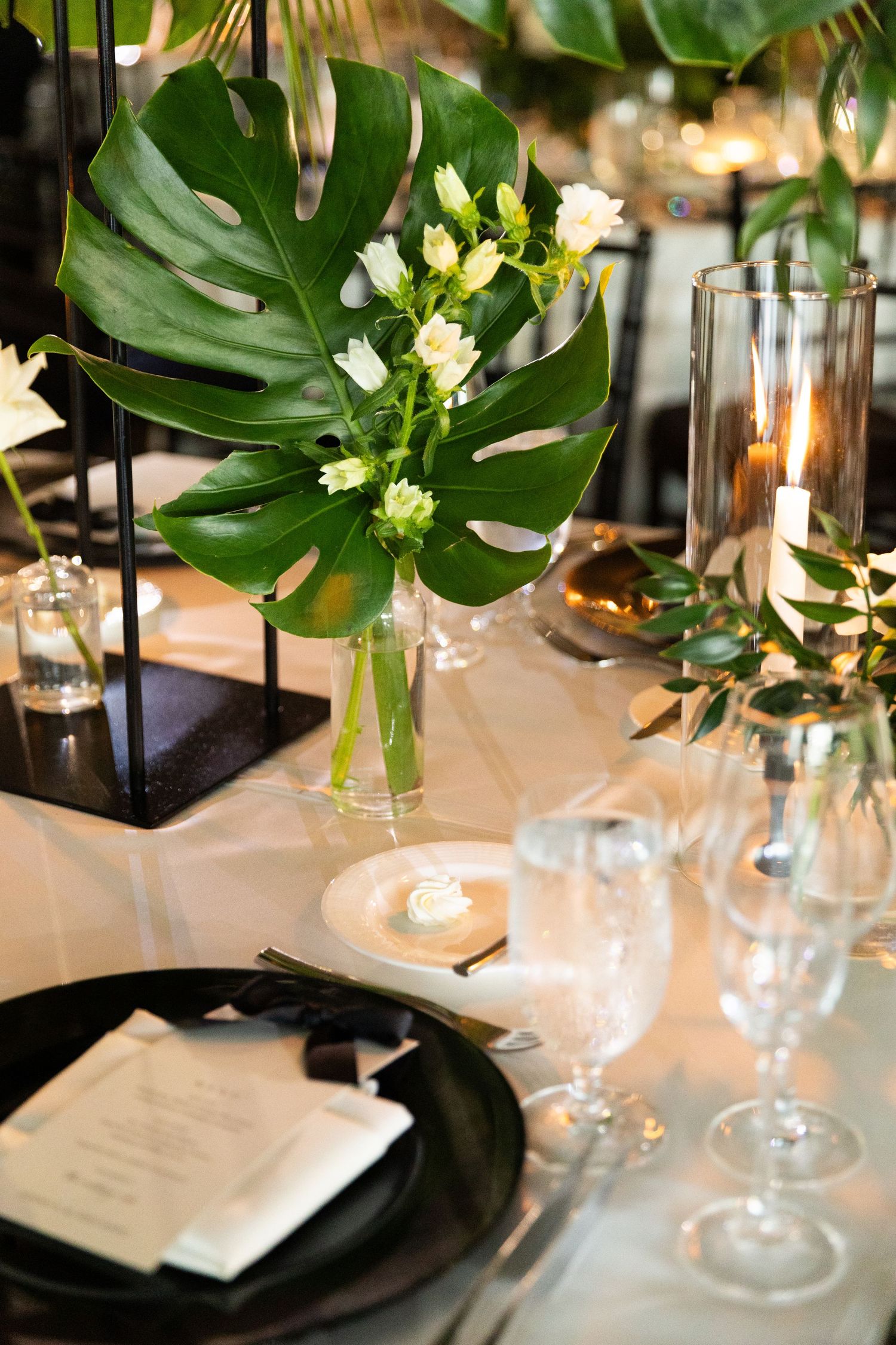 Elegant table setting with tropical monstera leaves and white floral centerpieces for a formal event.