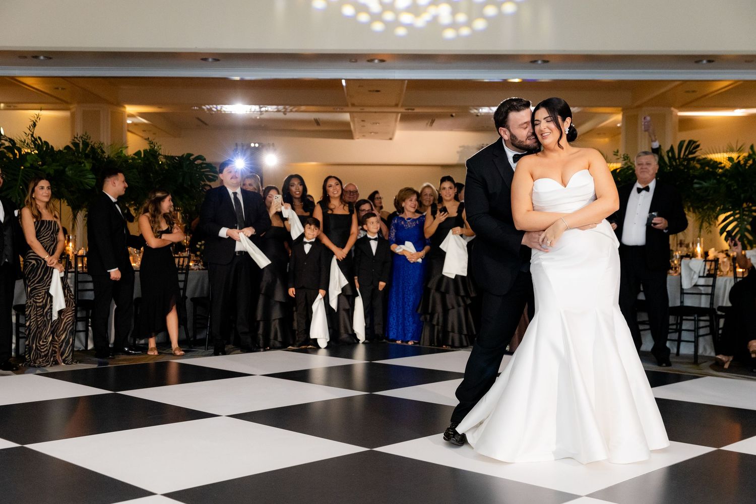 Wedding reception celebration with guests surrounding a couple on a black and white dance floor.