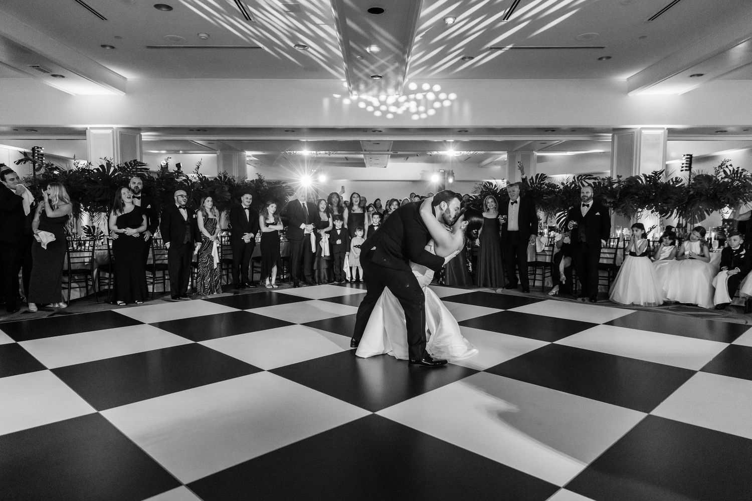 An elegant ballroom reception with a dramatic black and white checkered dance floor under crystal chandeliers.