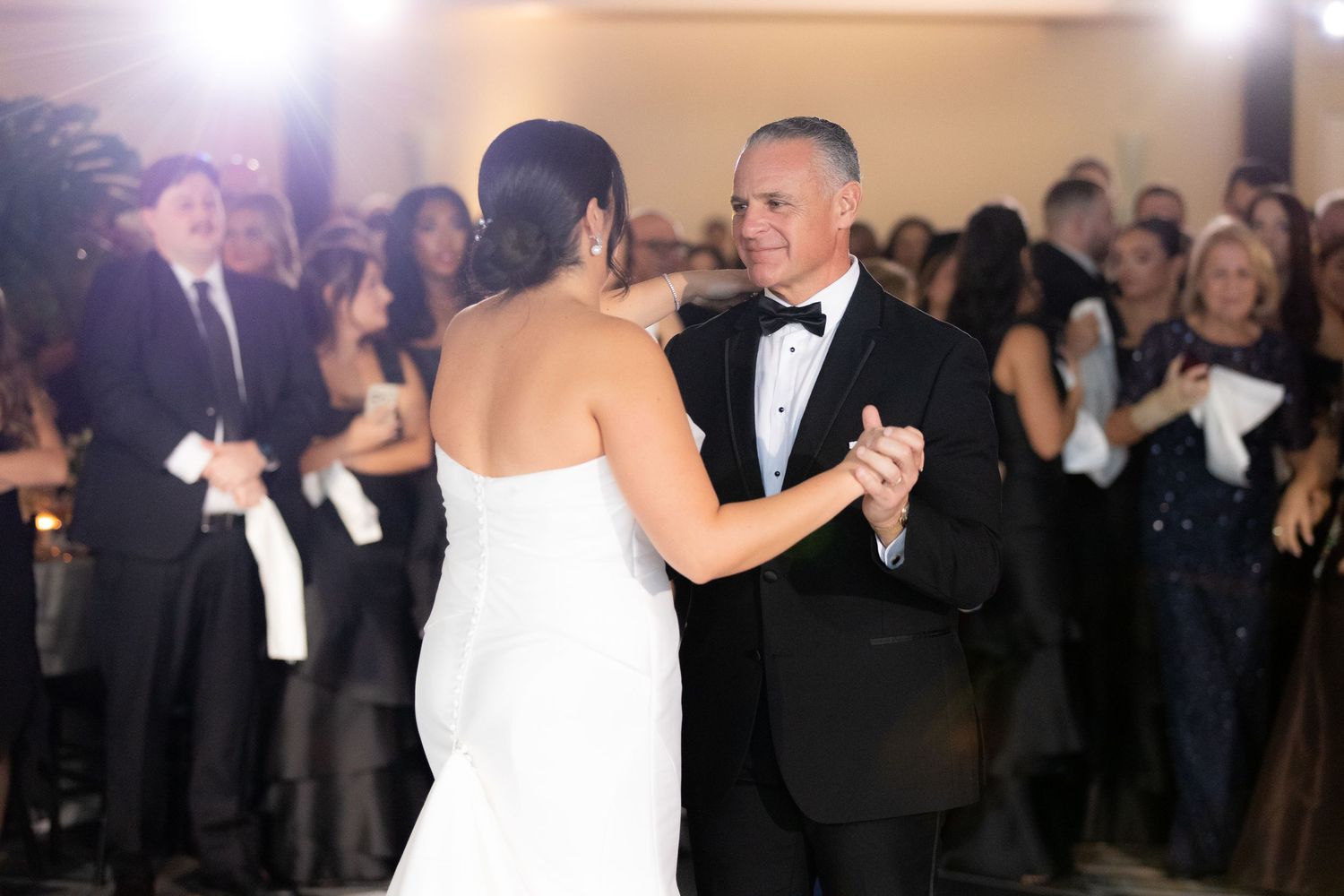 Romantic first dance moment at wedding reception with guests watching in background.